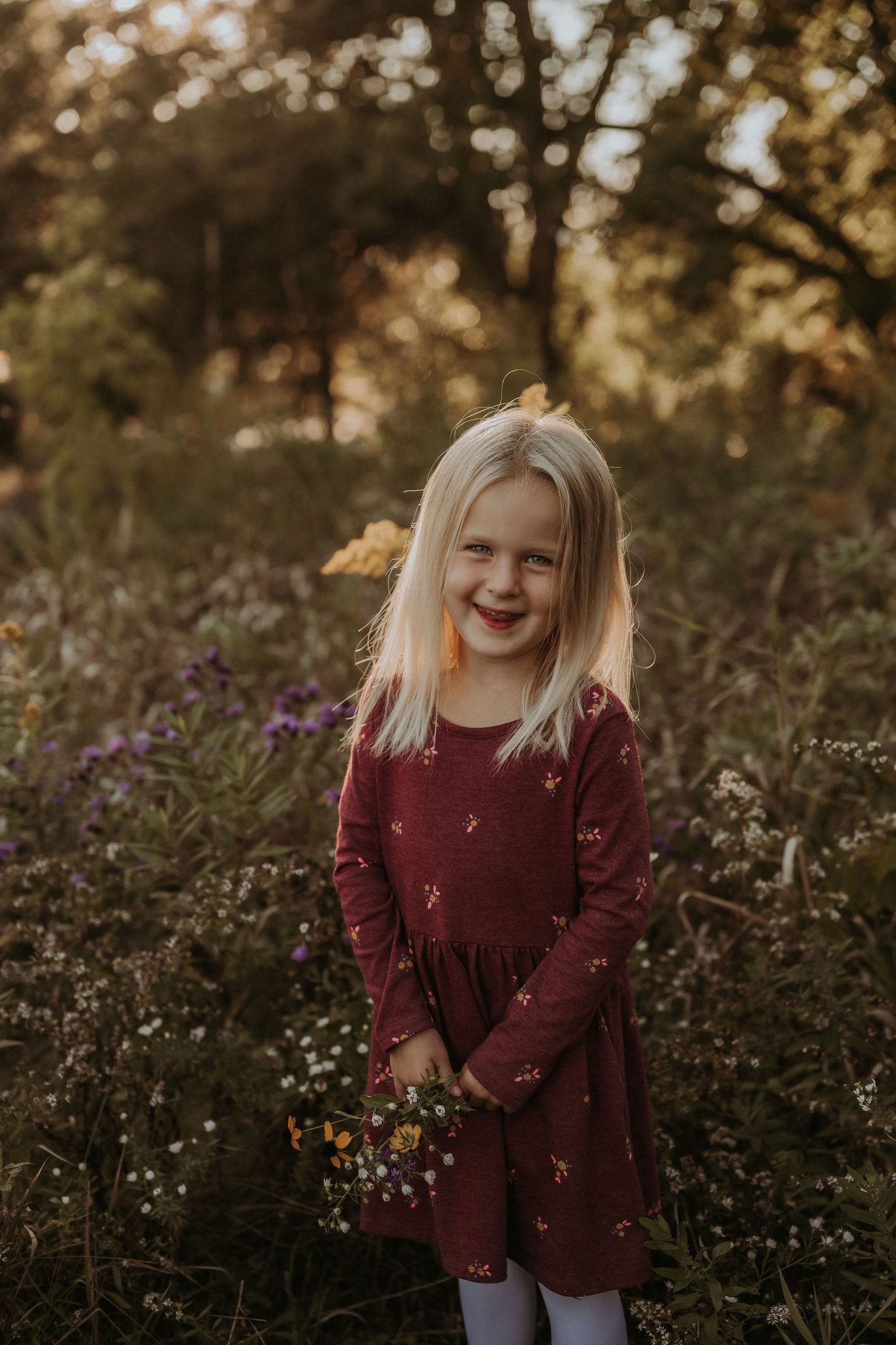 A joyful moment captured in a burgundy dress among wildflowers at sunset.