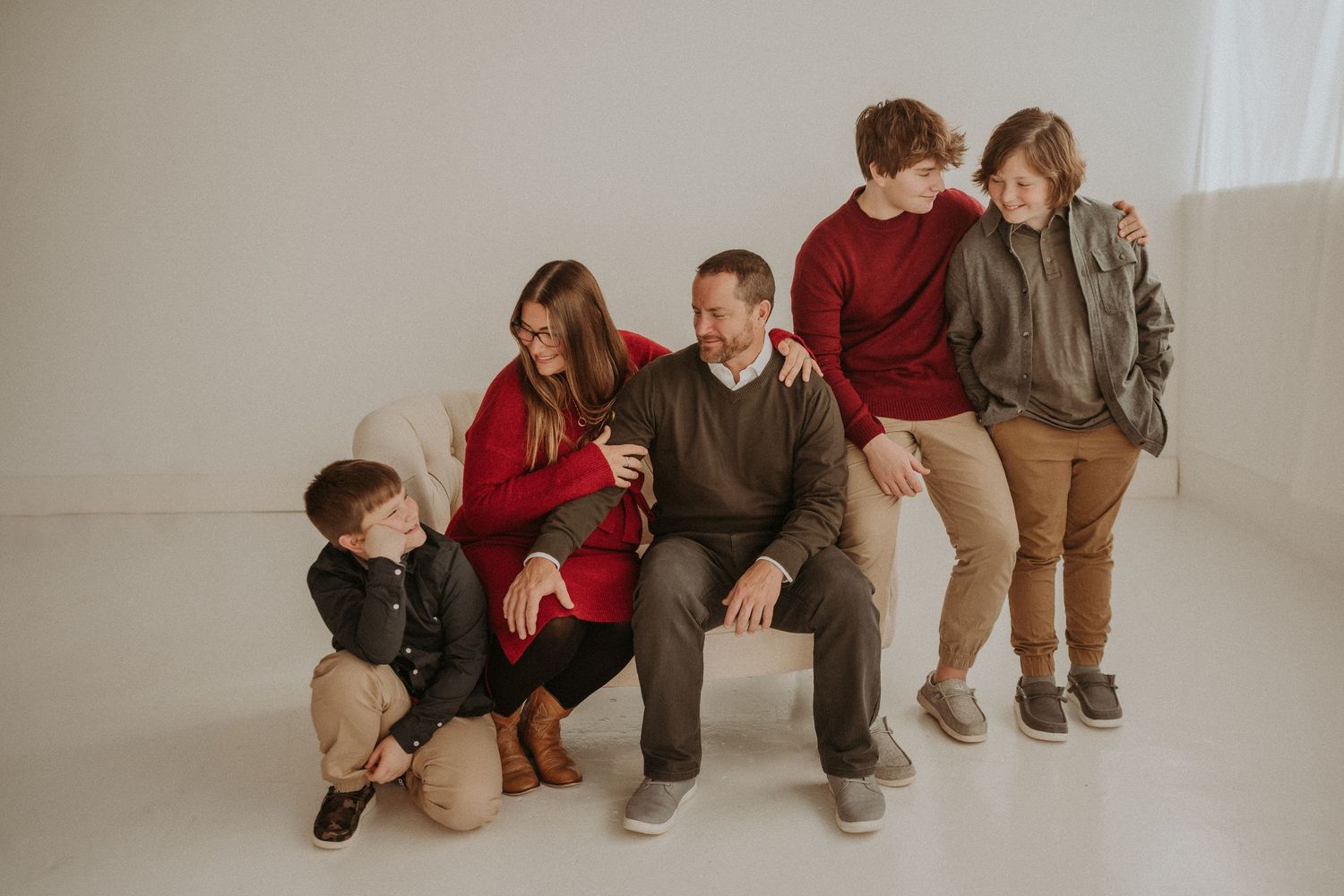 Family group seated together in casual attire against minimalist white studio background.