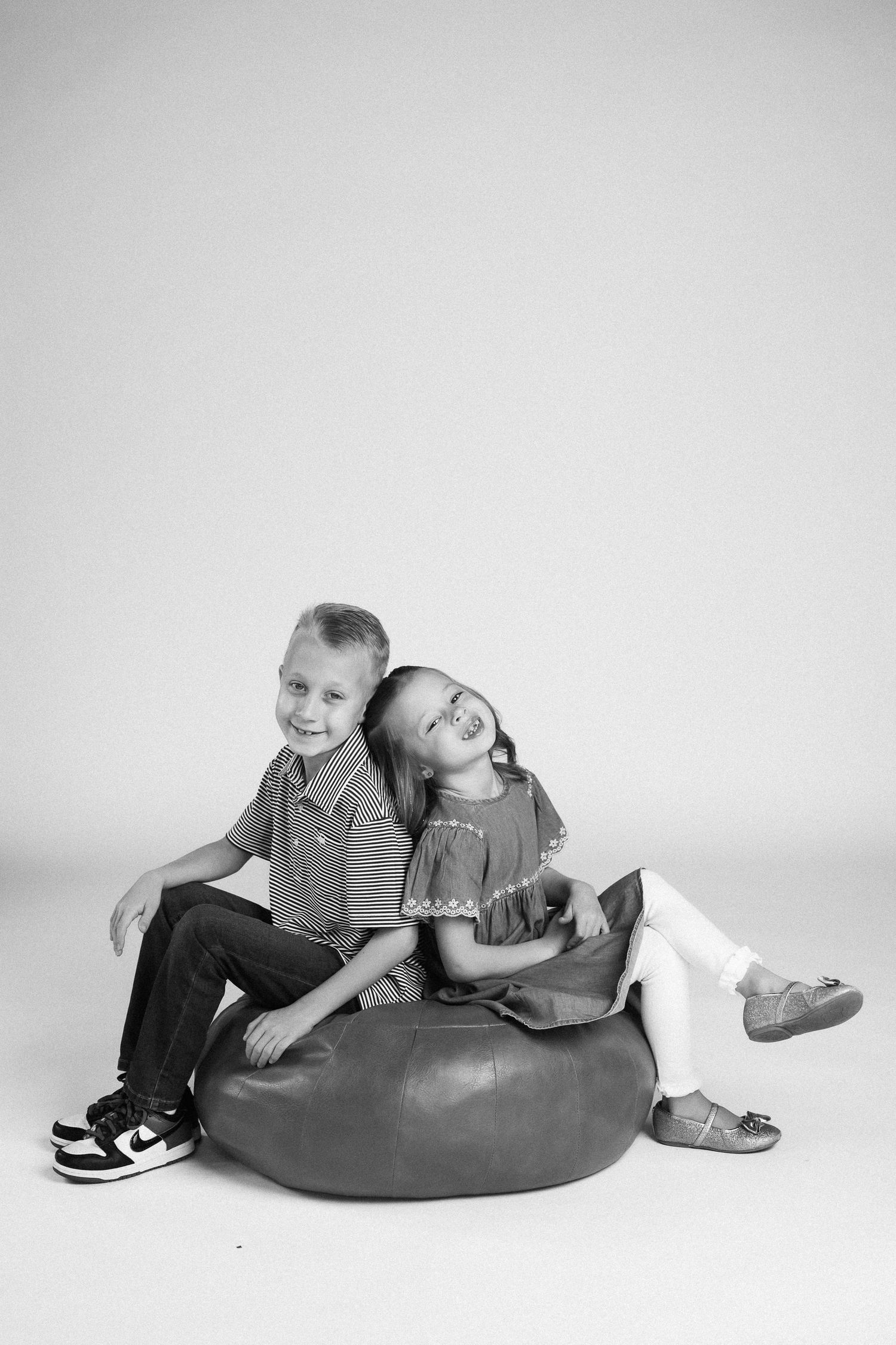 Black and white photos of two people relaxing and playing on a bean bag chair in casual attire.