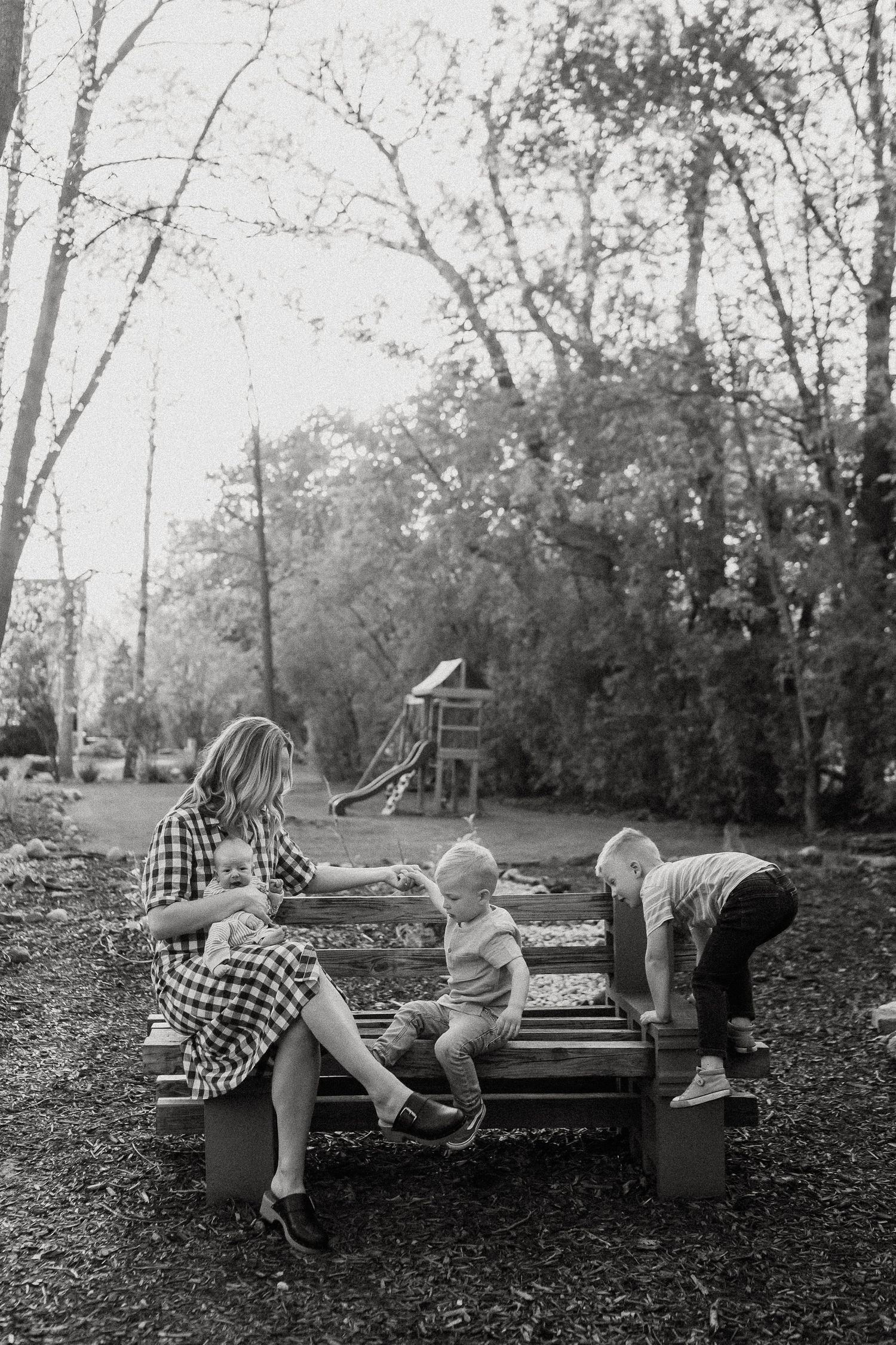 Black and white photo of a mother sitting on a bench with three young children in a backyard.
