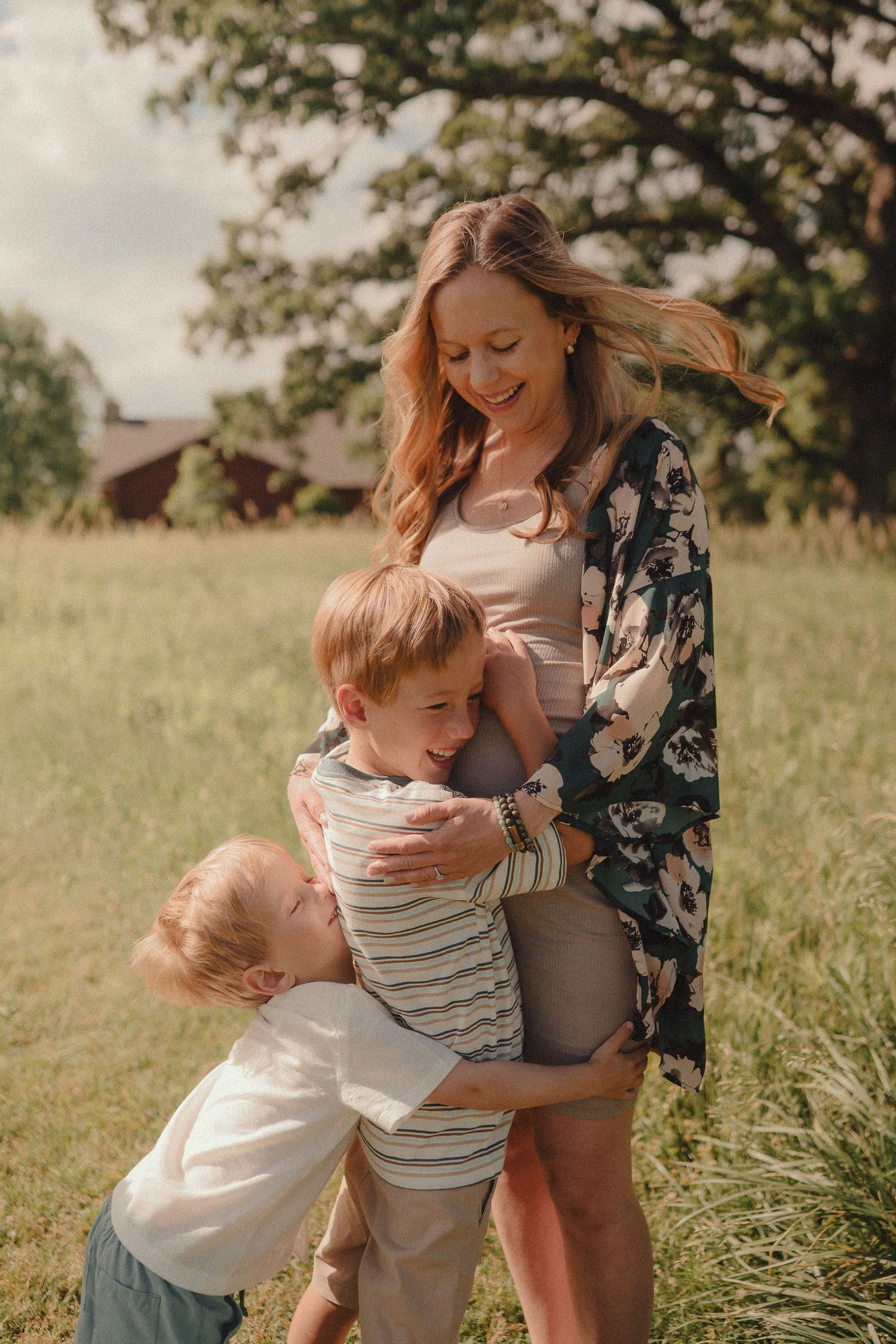 A smiling mother in a floral kimono embraces her two young children in a sunny green field.