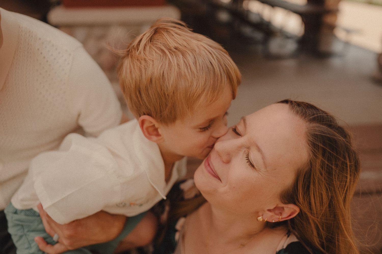 A young boy lovingly kisses his smiling mother on the cheek in a warm candid moment.