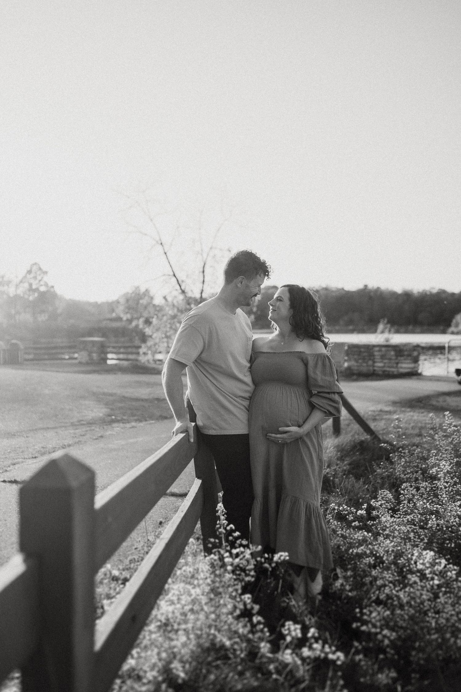 Couple in a tender embrace along a fence during golden hour.
