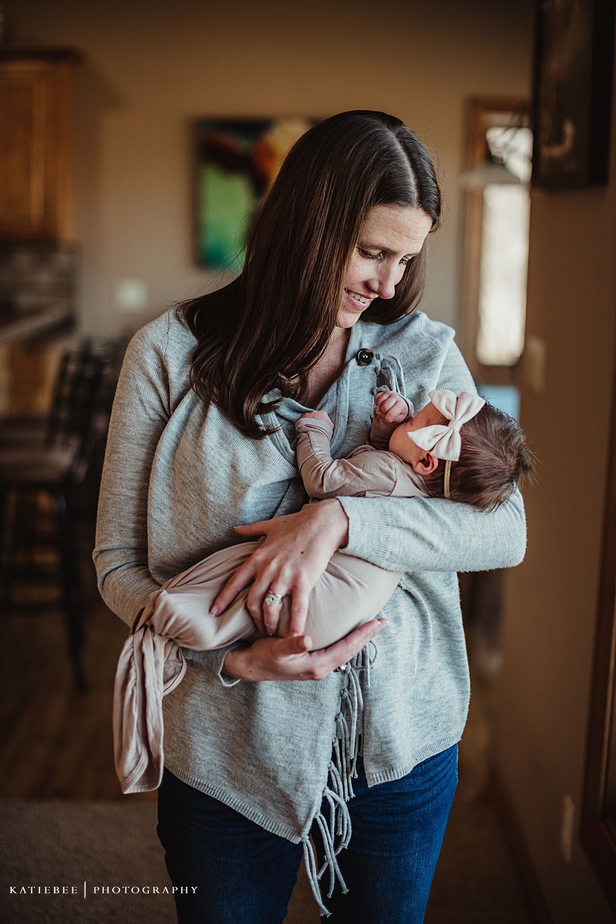 Indoor lifestyle photography of parent holding newborn baby in grey casual home setting.