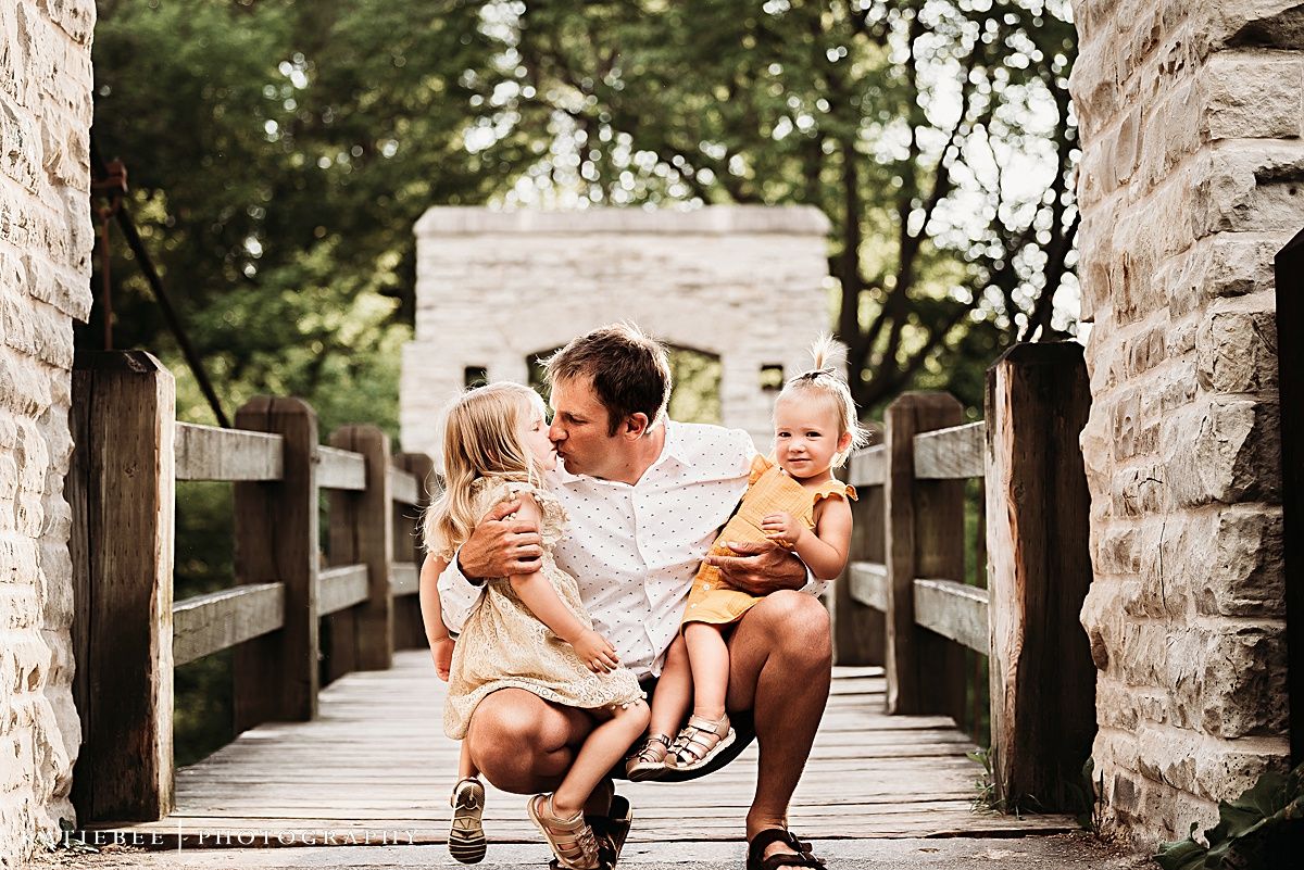 Family sharing a tender moment while sitting together on a wooden bridge.