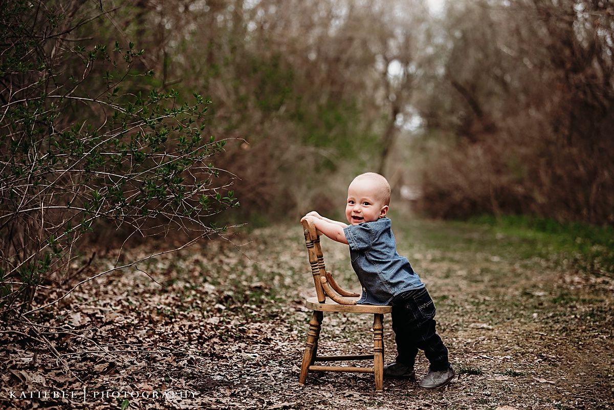 Small child in blue shirt playing with wooden chair on forest path.