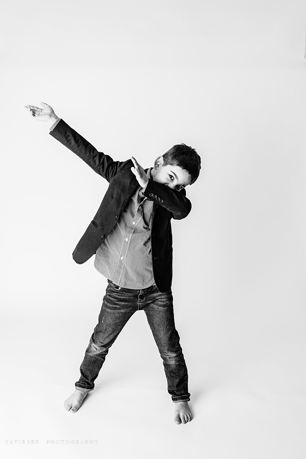 Black and white image of child in blazer striking dynamic dance pose with raised arm.