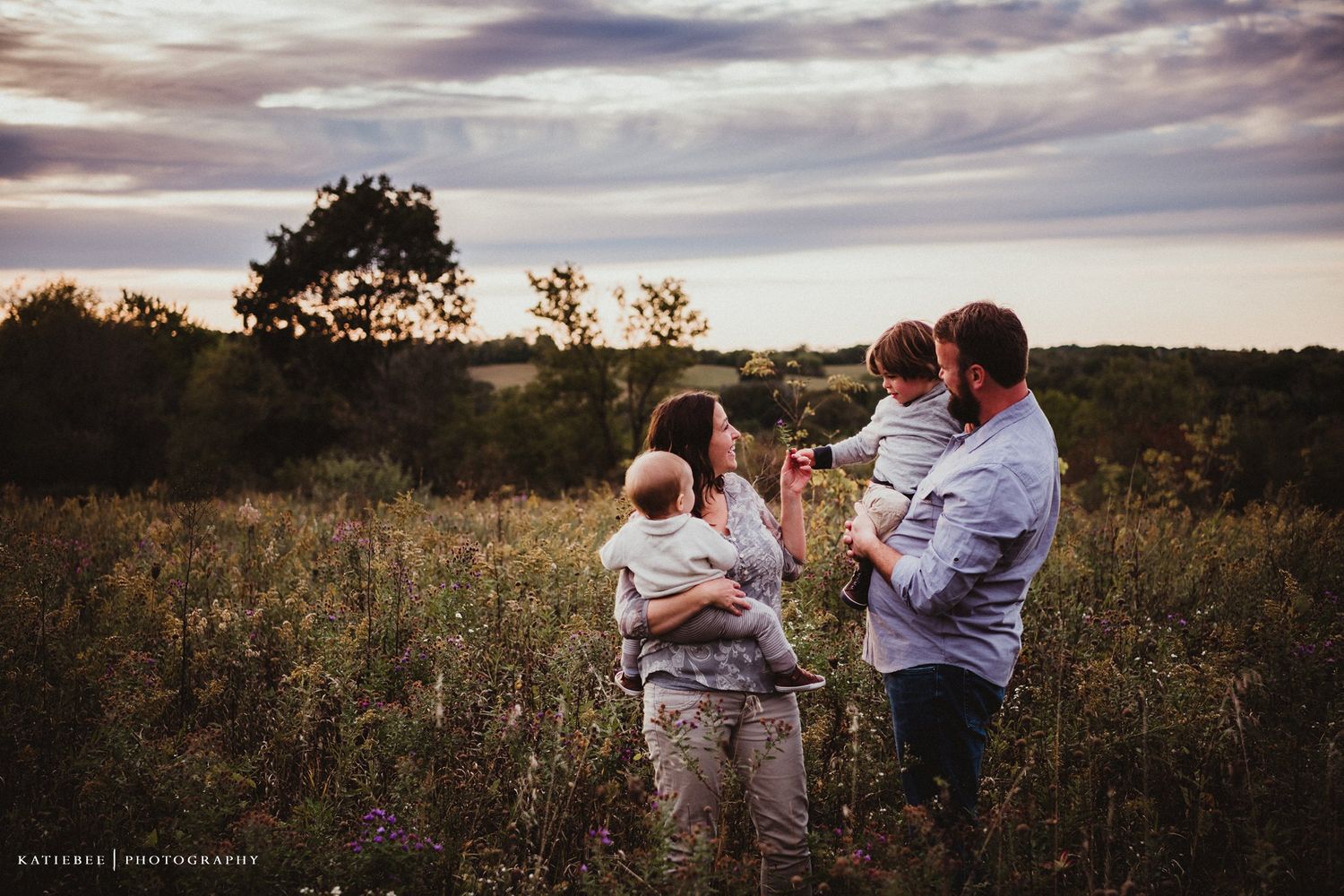 Family embraces during golden hour in rustic field setting.