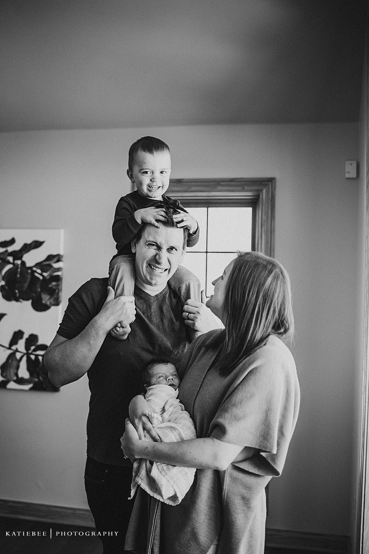 Black and white candid family portrait showing playful interaction by window.