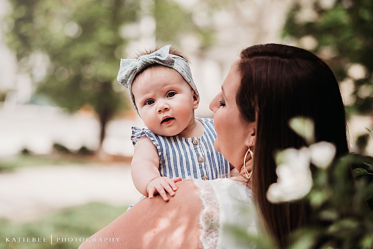 A baby in striped outfit and headband shares a sweet moment with caregiver outdoors.