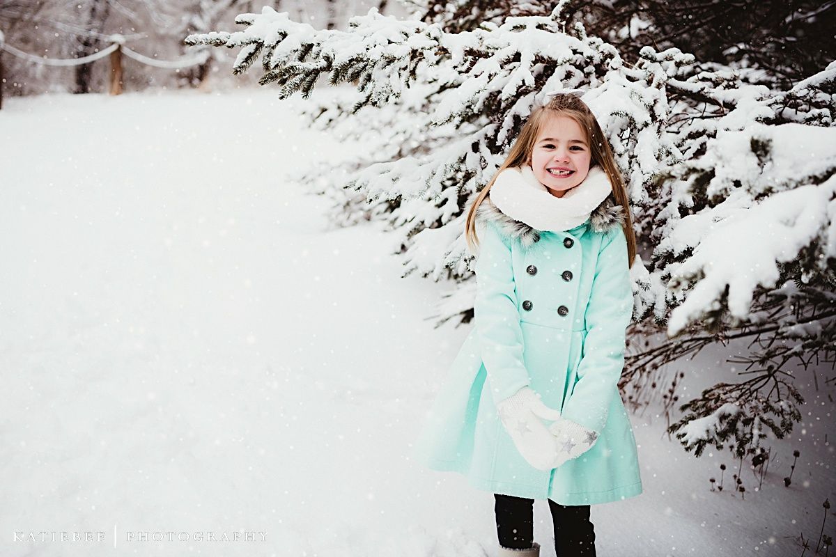 Person in mint winter coat playing in snowy landscape.
