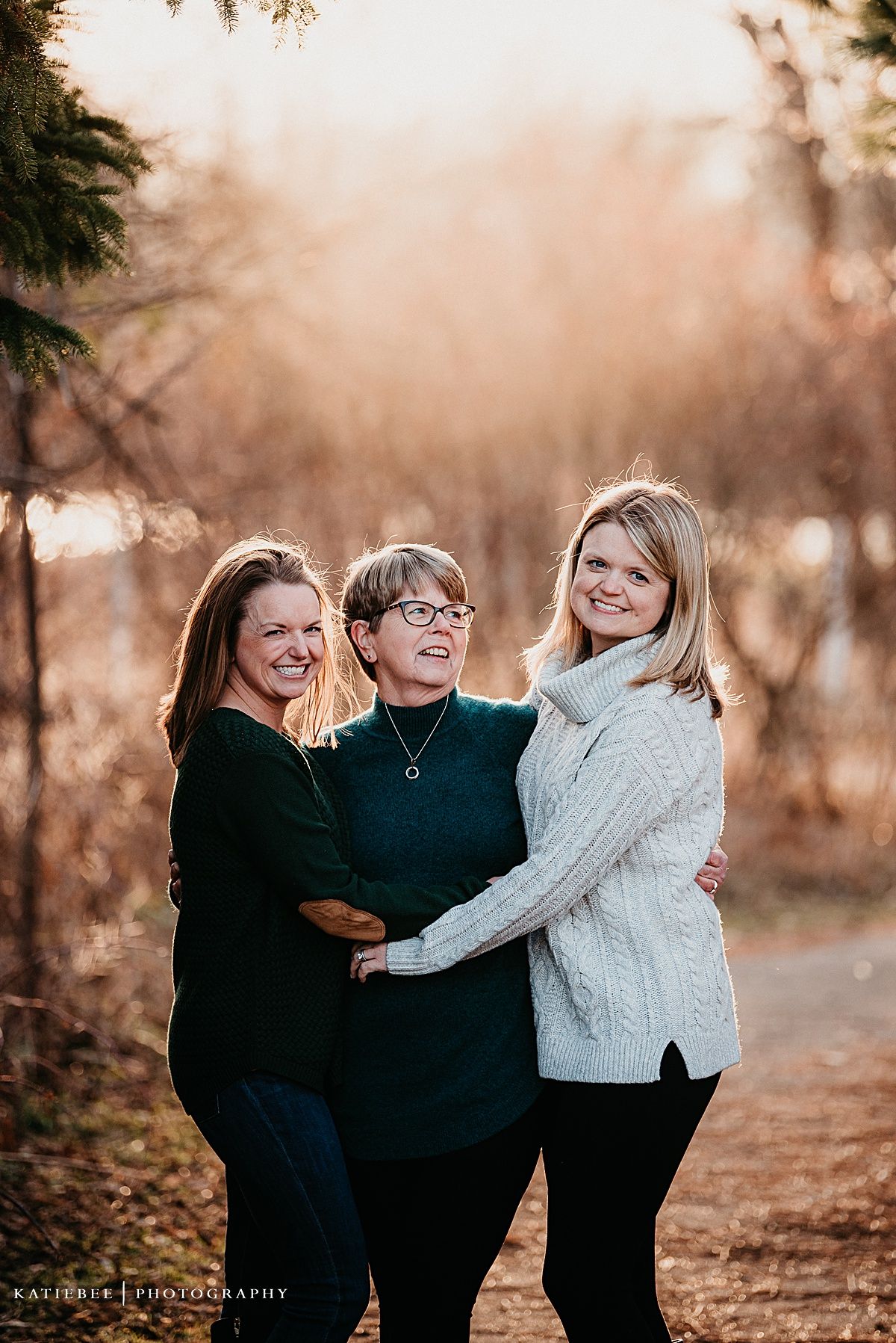 Three people share a warm embrace while laughing together on an autumn trail.
