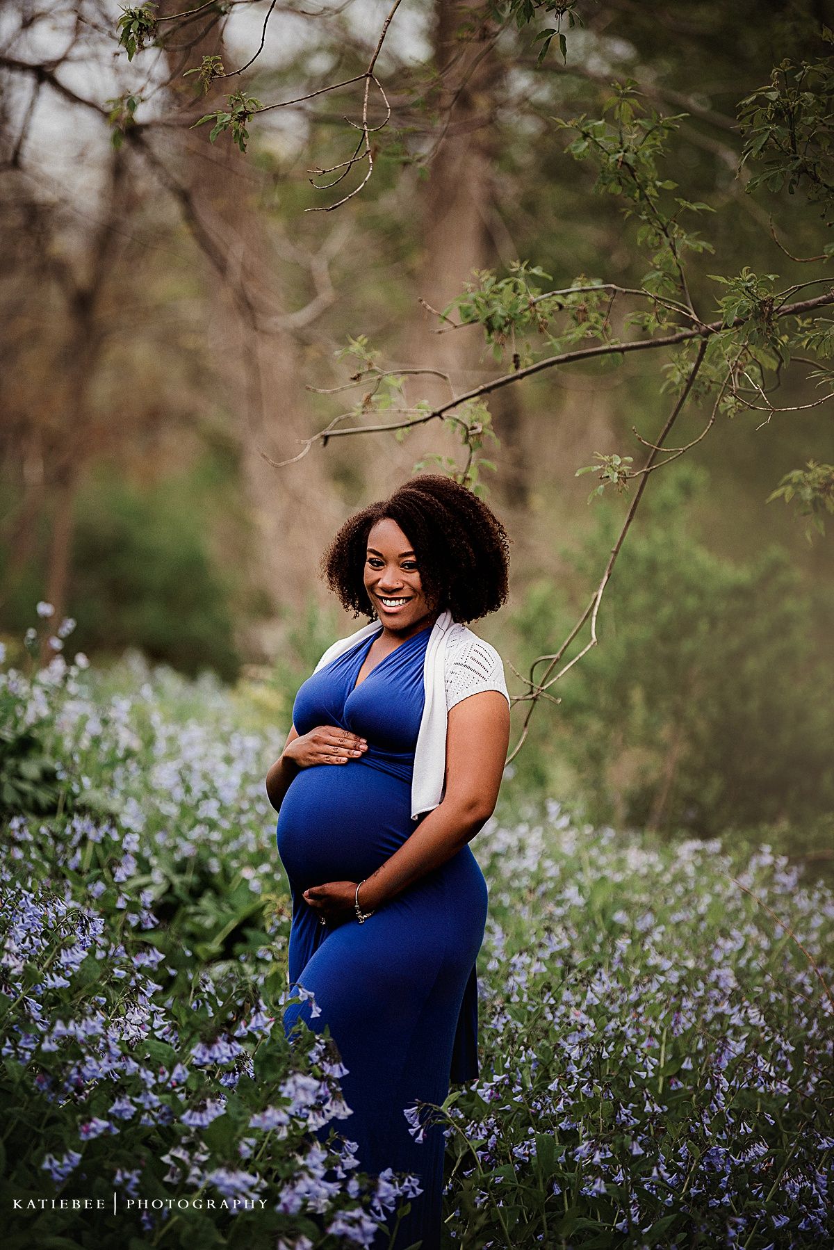 Glowing maternity portrait amid purple wildflowers showing expectant parent in blue dress.