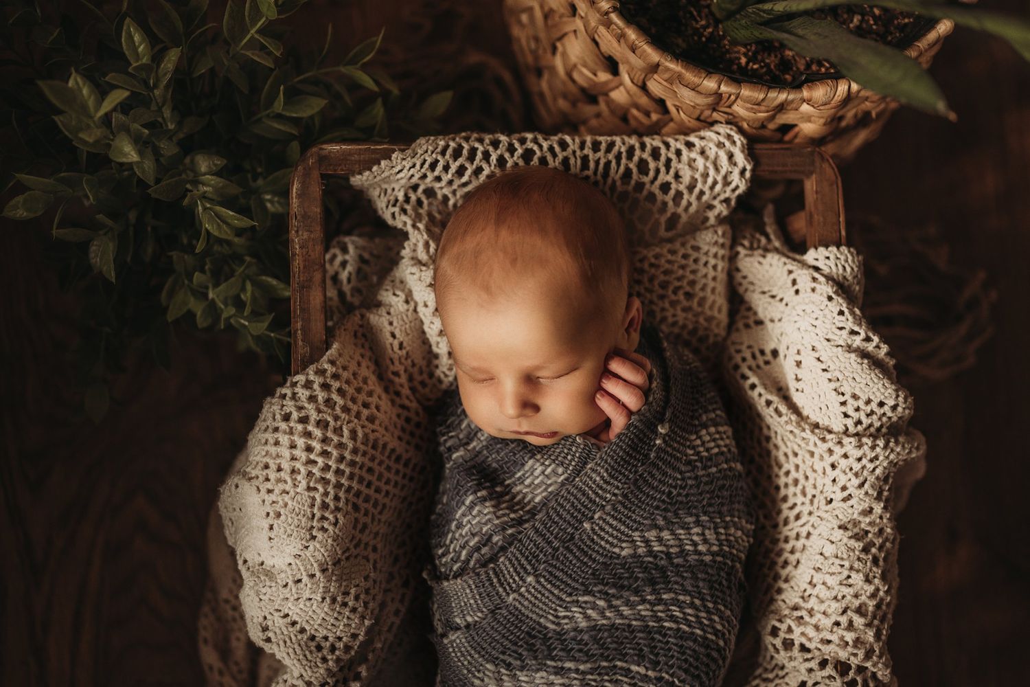 Overhead view of a sleeping baby wrapped in gray knitted blankets on a wooden surface.