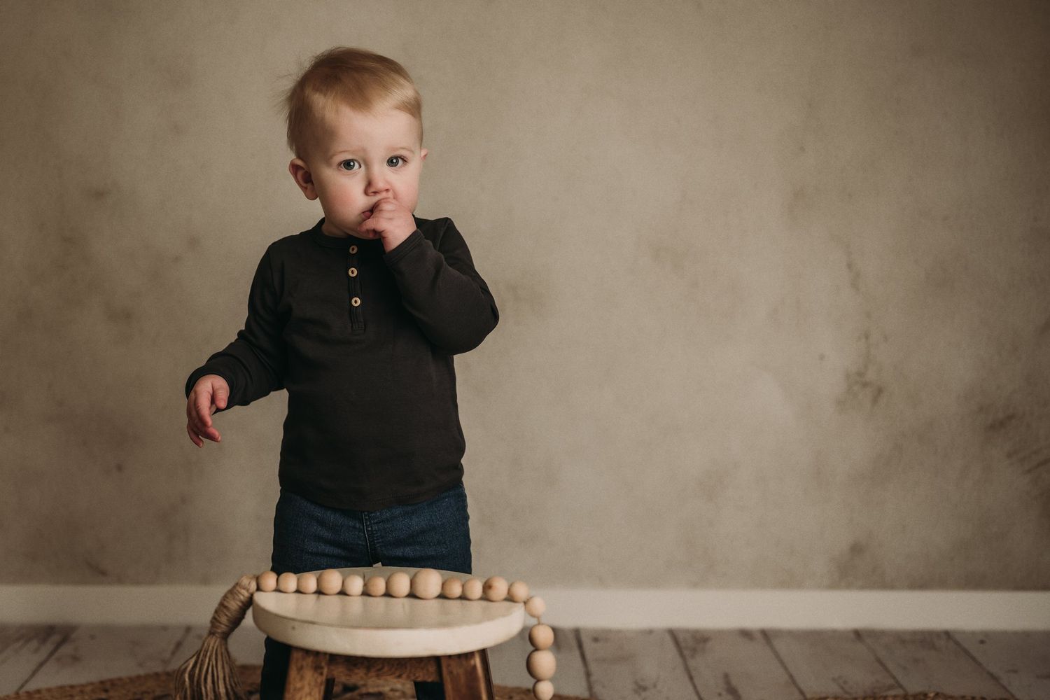 Lifestyle portrait of a toddler in black henley looking at a wooden toy ring.