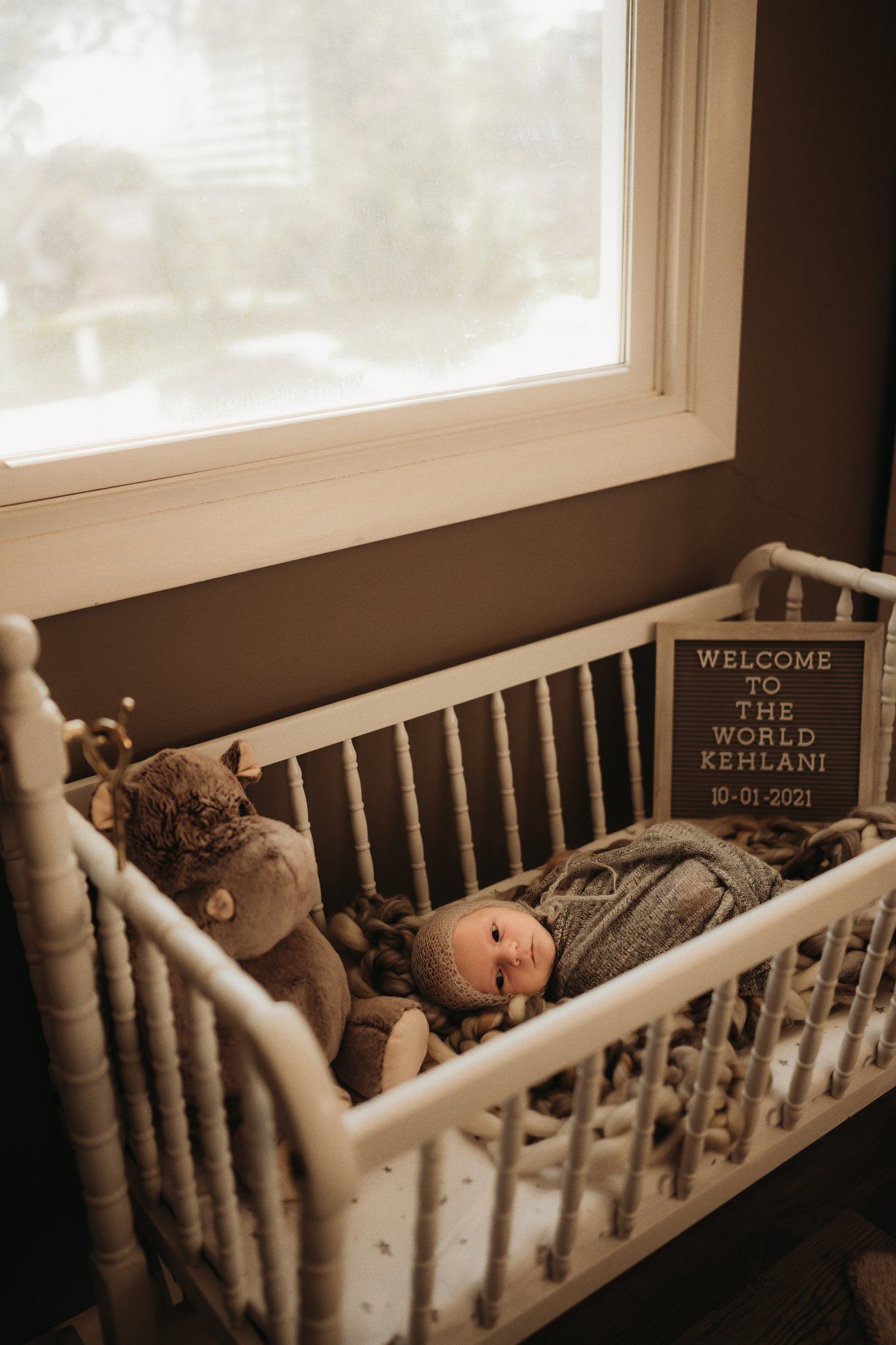 White vintage crib with stuffed animal and welcome sign by bright window.