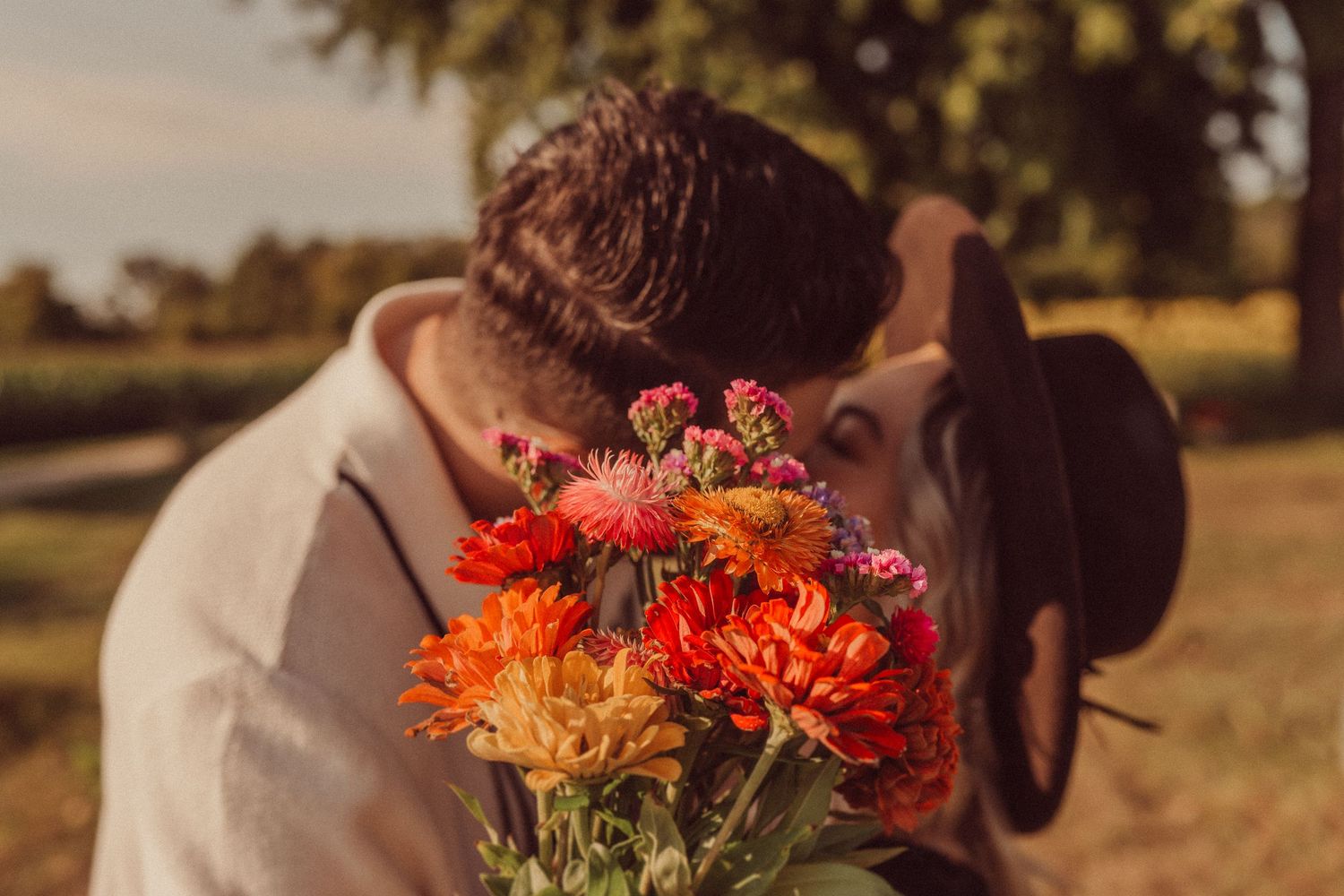 Couple sharing an intimate moment behind a vibrant bouquet of orange and pink flowers.