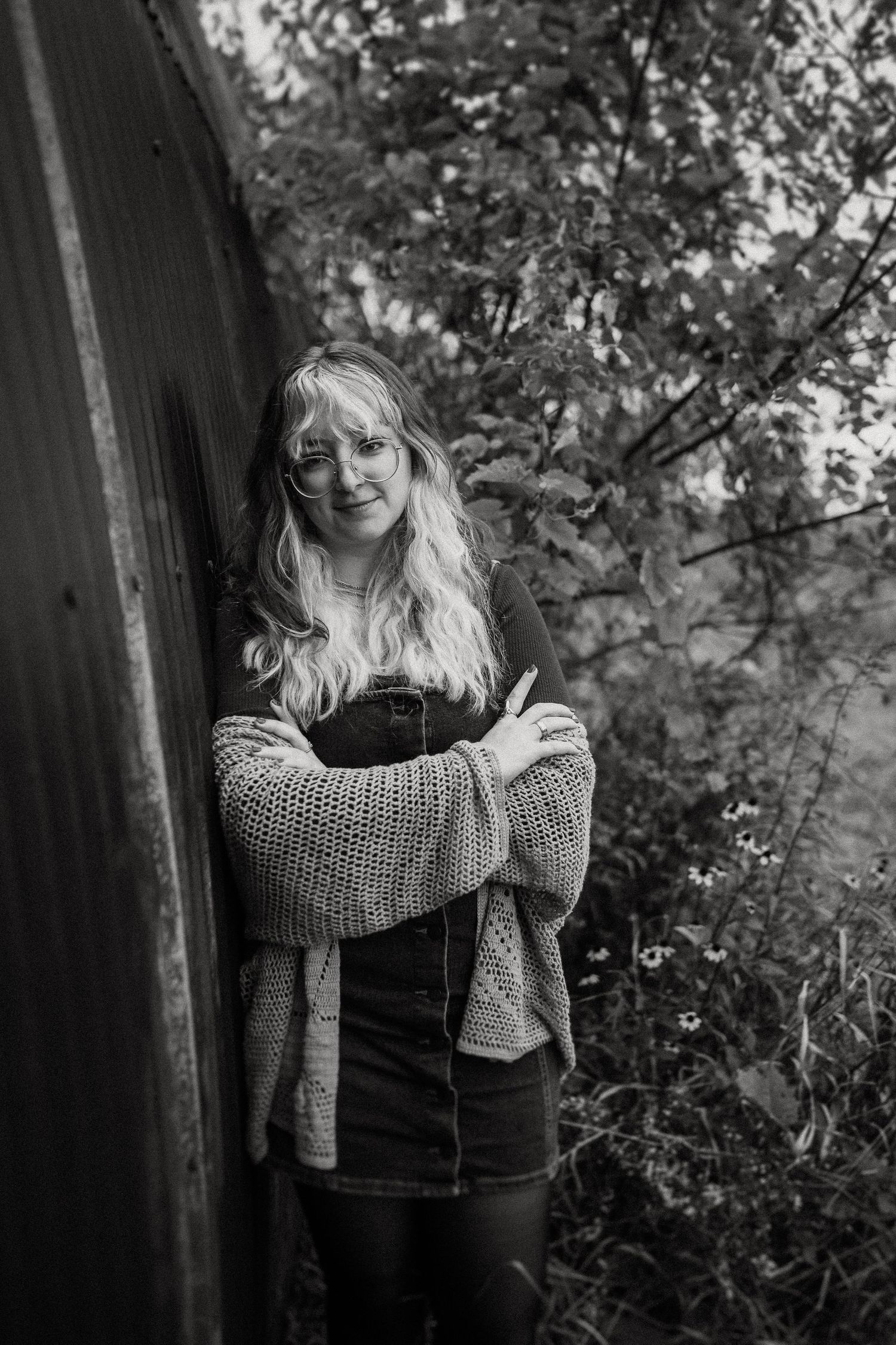 Black and white portrait against curved metal wall with natural foliage background.