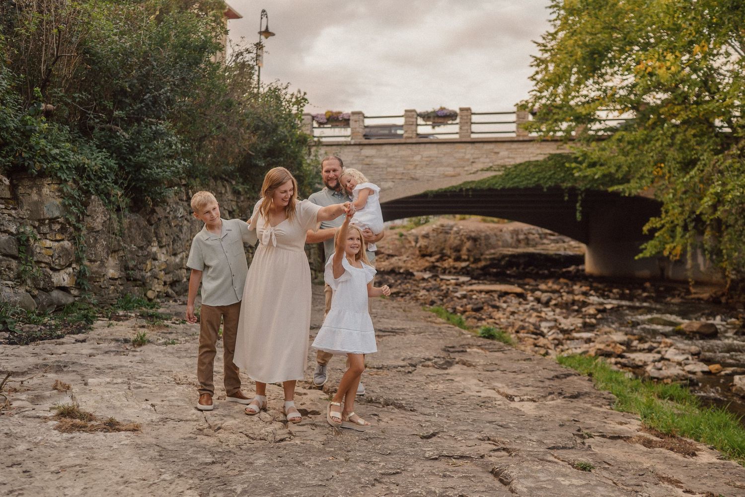 A family walks together on rocky terrain near a stone bridge during golden hour.