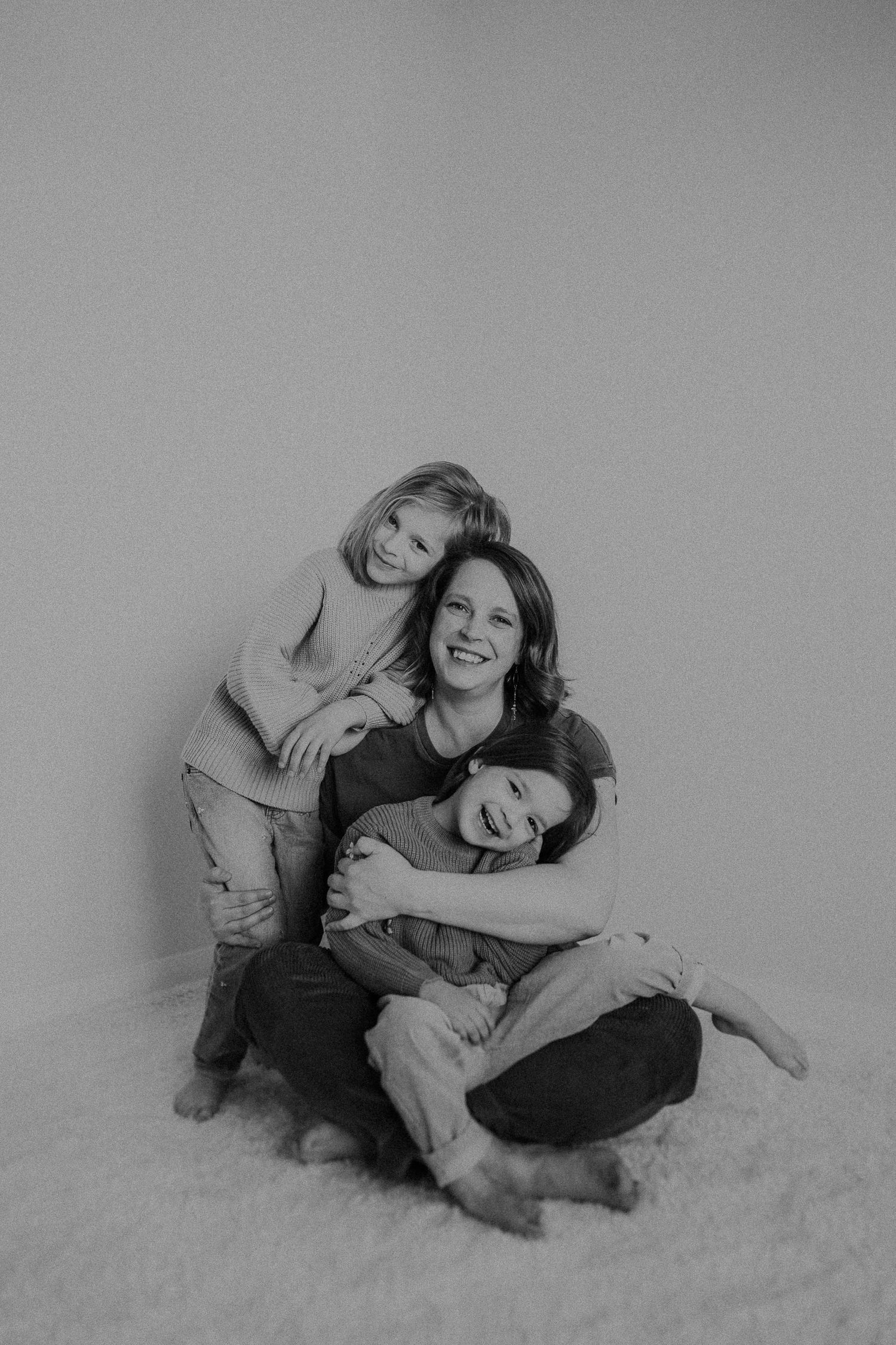 Black and white portrait showing affectionate embrace and genuine smiles against neutral background.