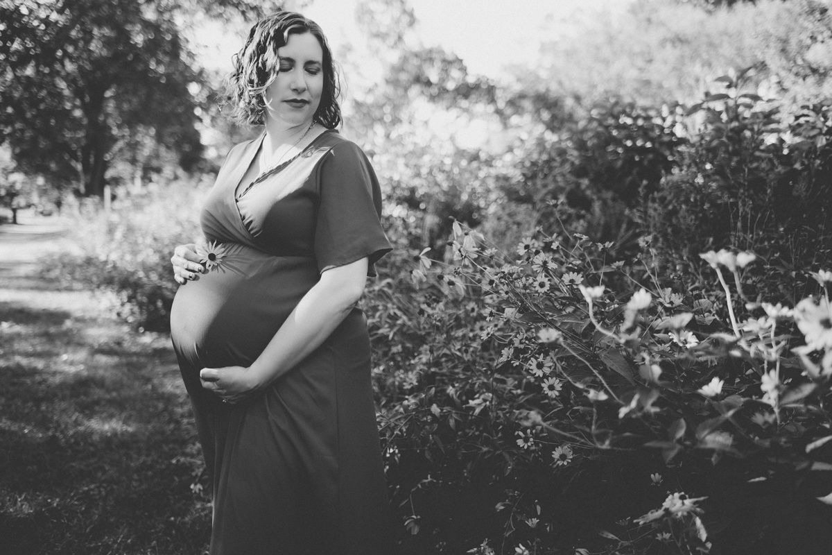 Black and white maternity photo of an expectant mother in a garden setting.