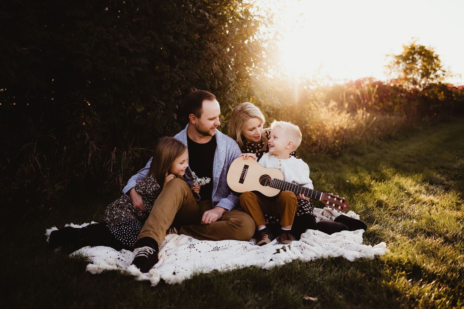 Family enjoying a tender outdoor moment while sitting on blanket during golden hour sunset.