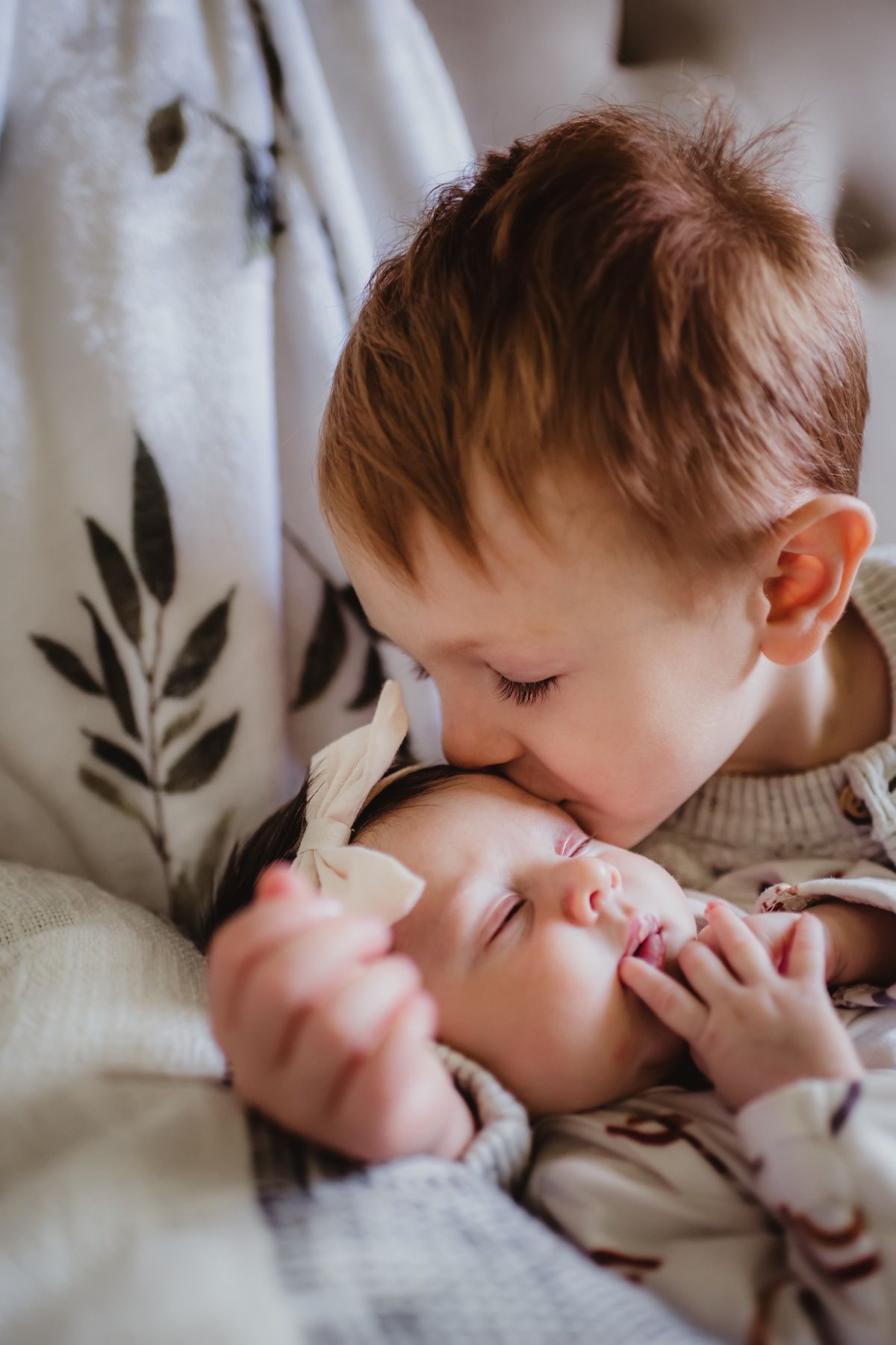 Intimate closeup of siblings sharing gentle moment against floral backdrop.