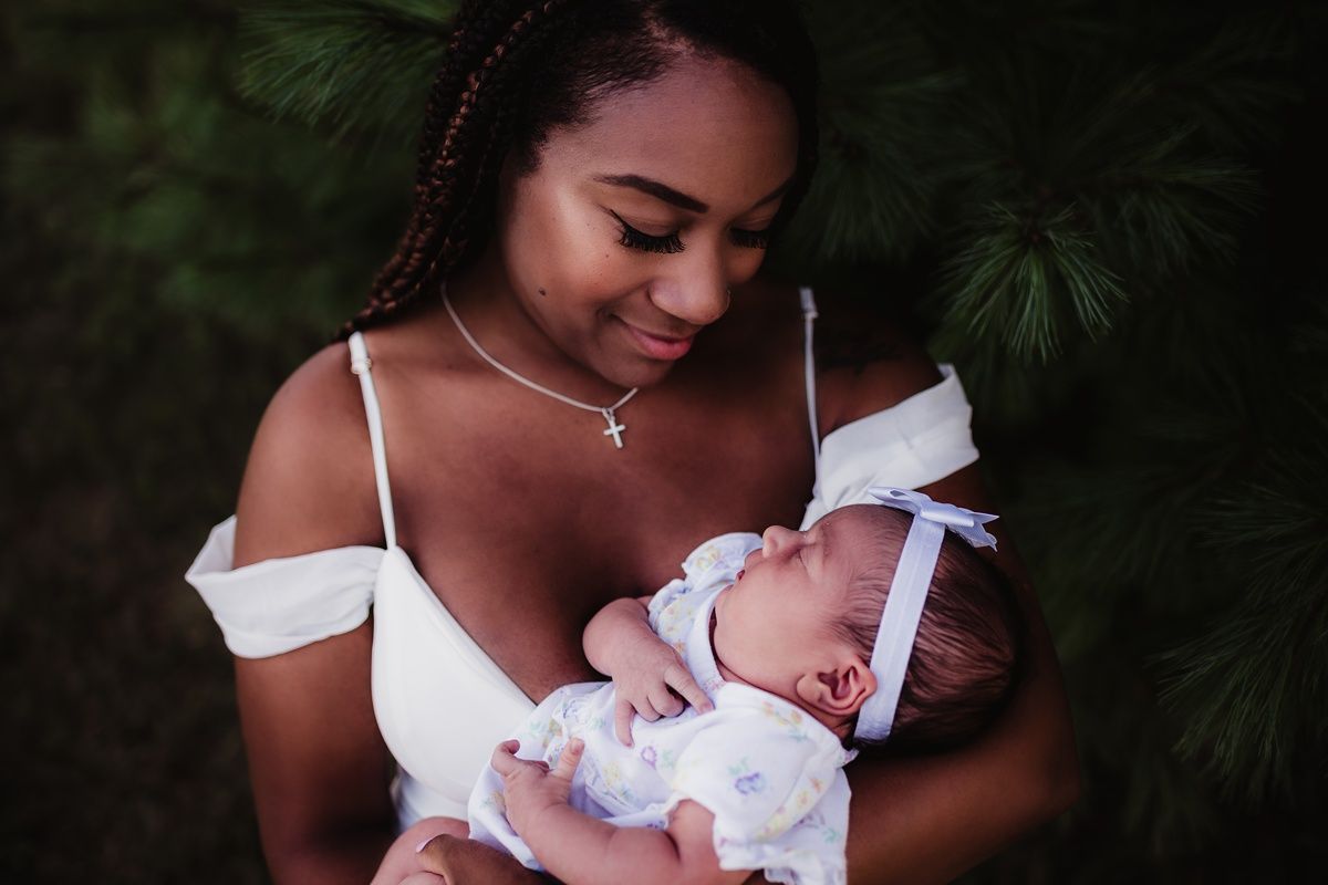 Tender moment captured between parent and newborn baby against natural outdoor backdrop.