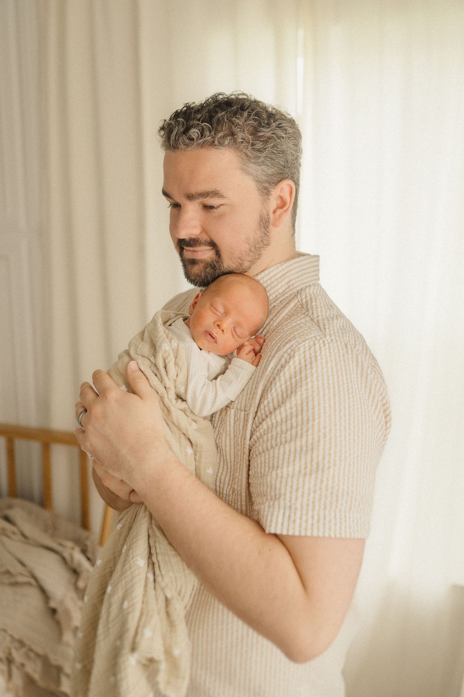 A tender moment as a parent in a beige striped shirt cradles their sleeping newborn baby against their chest.