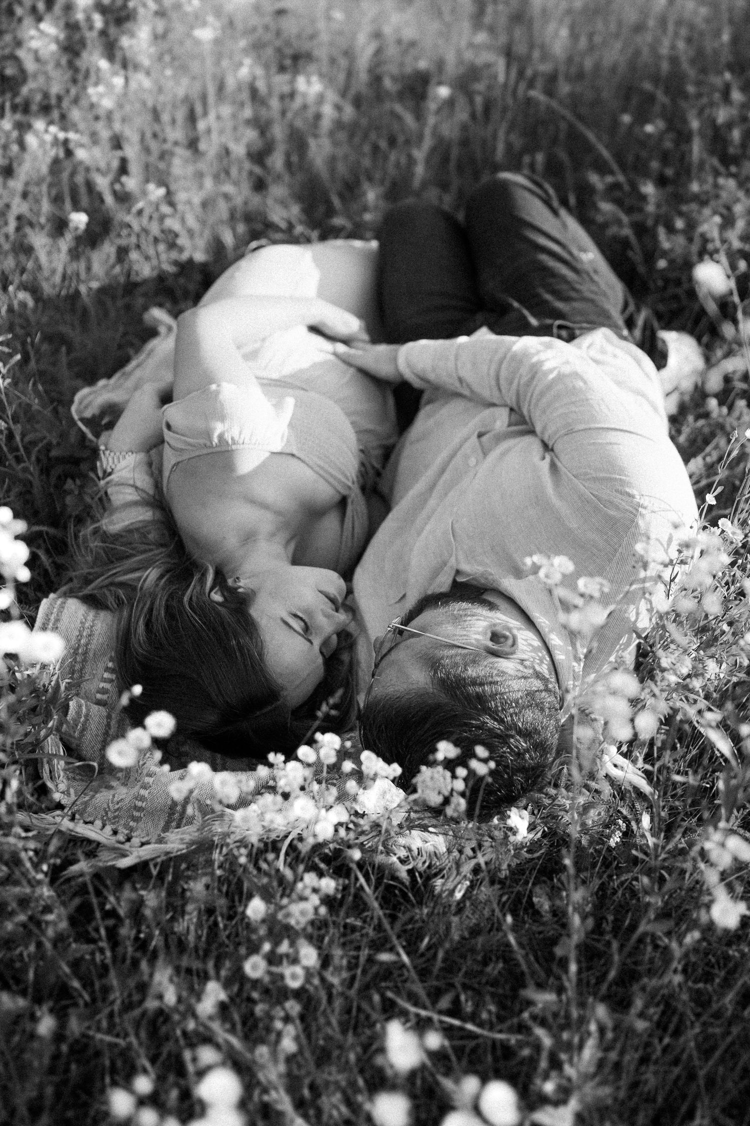Black and white image of a couple lying in a meadow surrounded by delicate wildflowers.