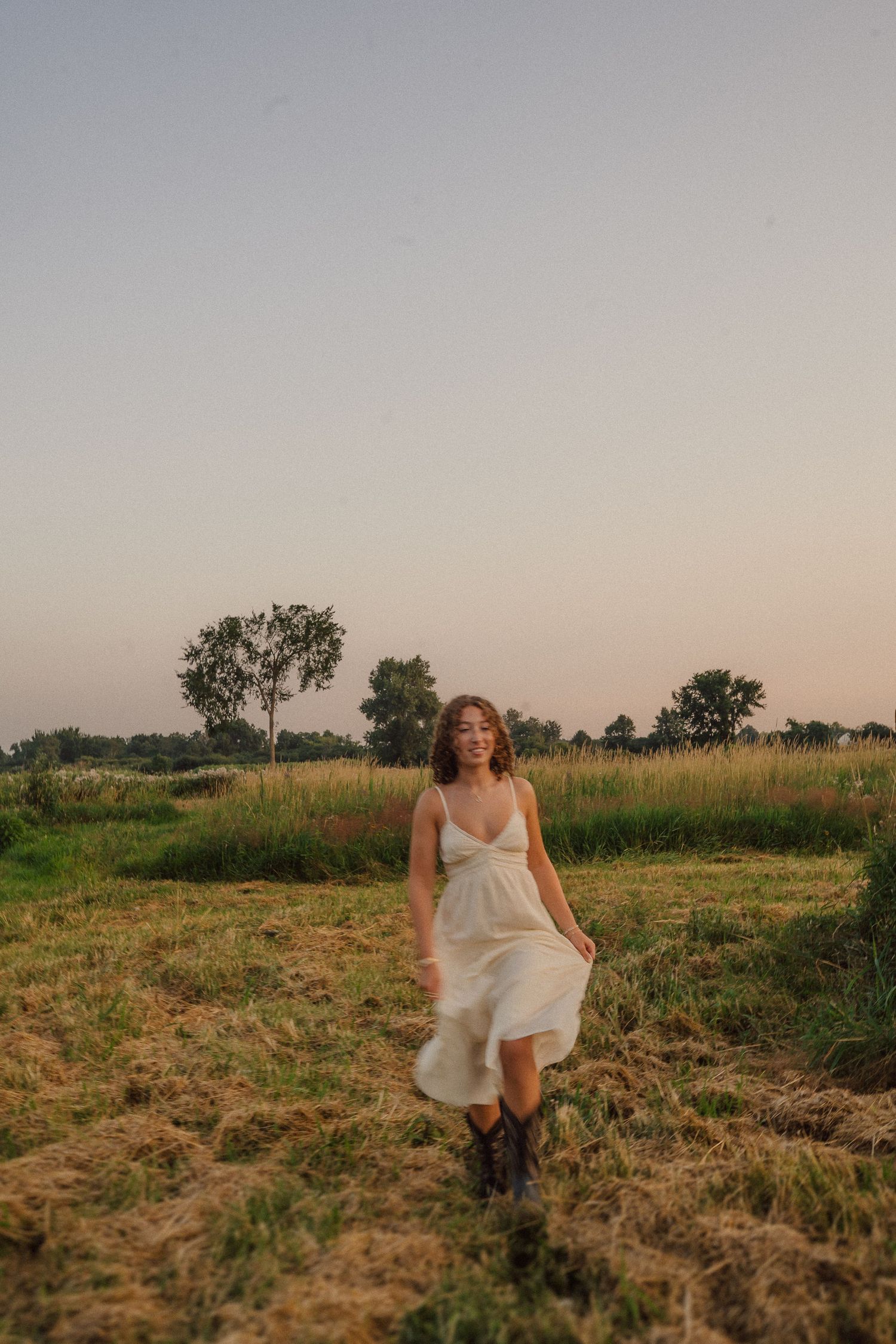 Figure in white dress running through a golden field at sunset against a soft sky.
