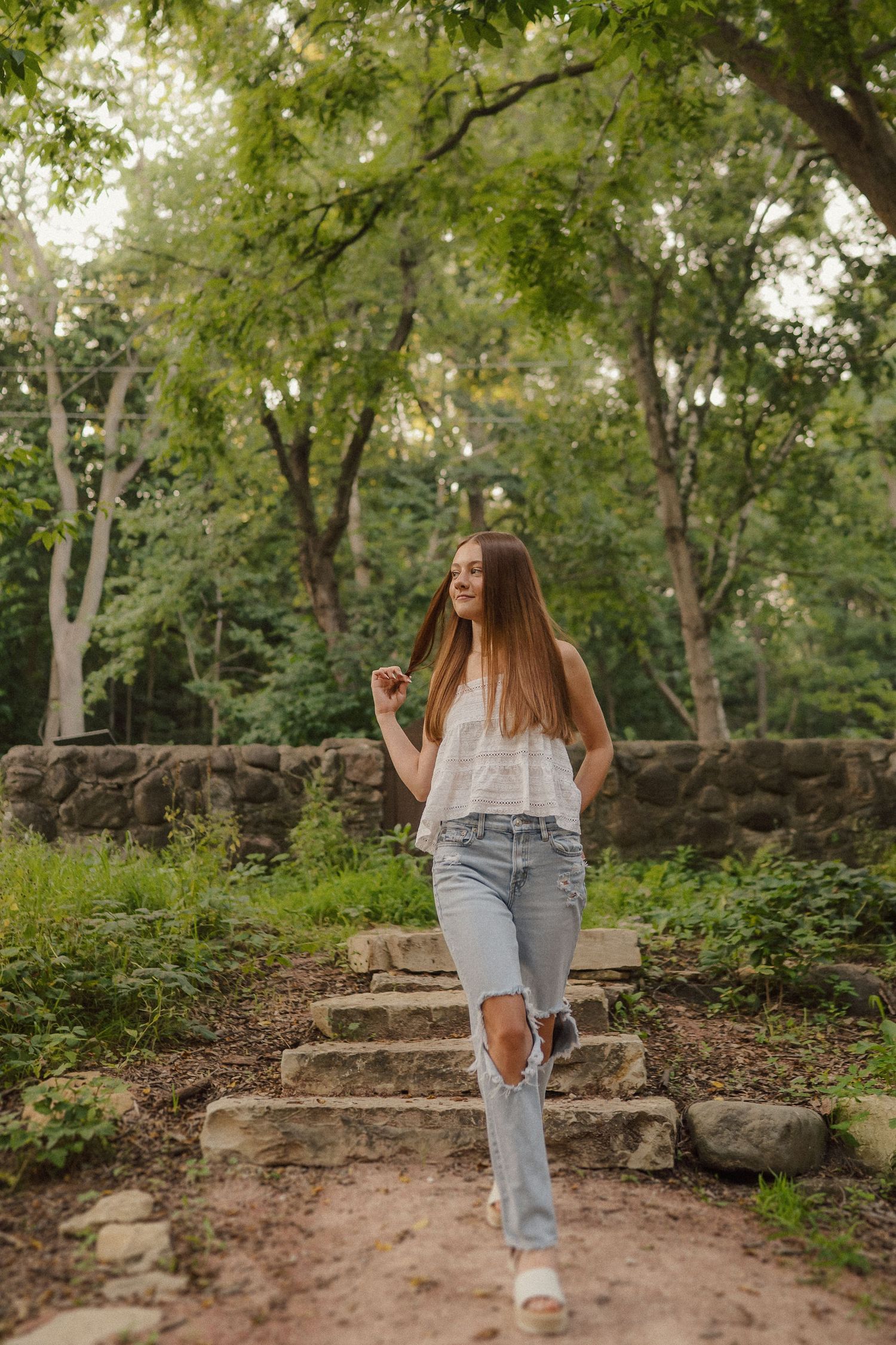 Person walks along stone steps surrounded by lush green trees in a garden setting.