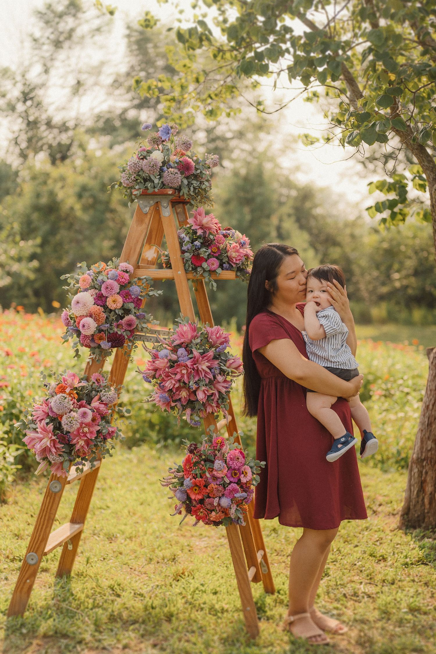 Wooden ladder adorned with pink and purple floral arrangements creates a whimsical outdoor scene in a sunlit garden.