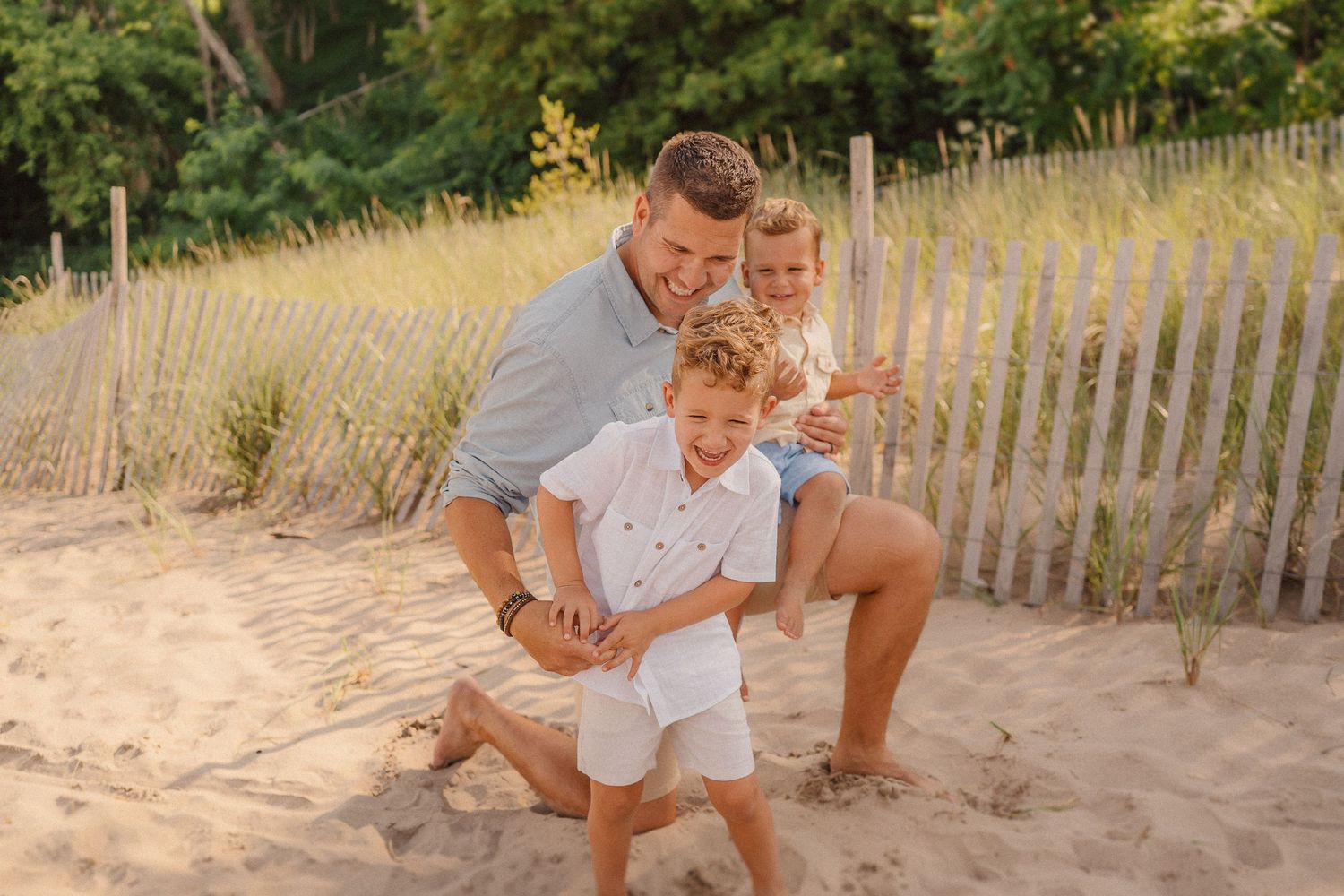 A joyful family portrait on sandy beach with wooden fence in background during golden hour.