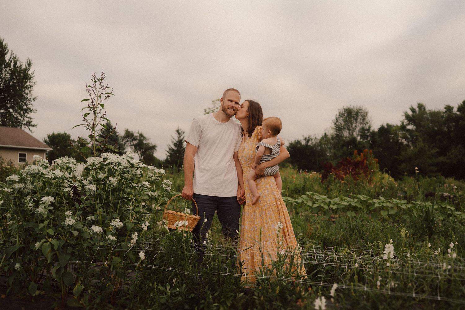 A romantic couple embraces in a lush field of wildflowers and tall grass at sunset creating an intimate silhouette.