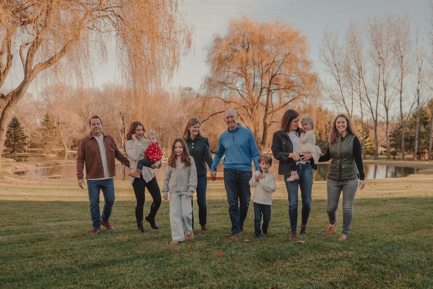 Family group walking together on a grassy hill during golden hour sunset.