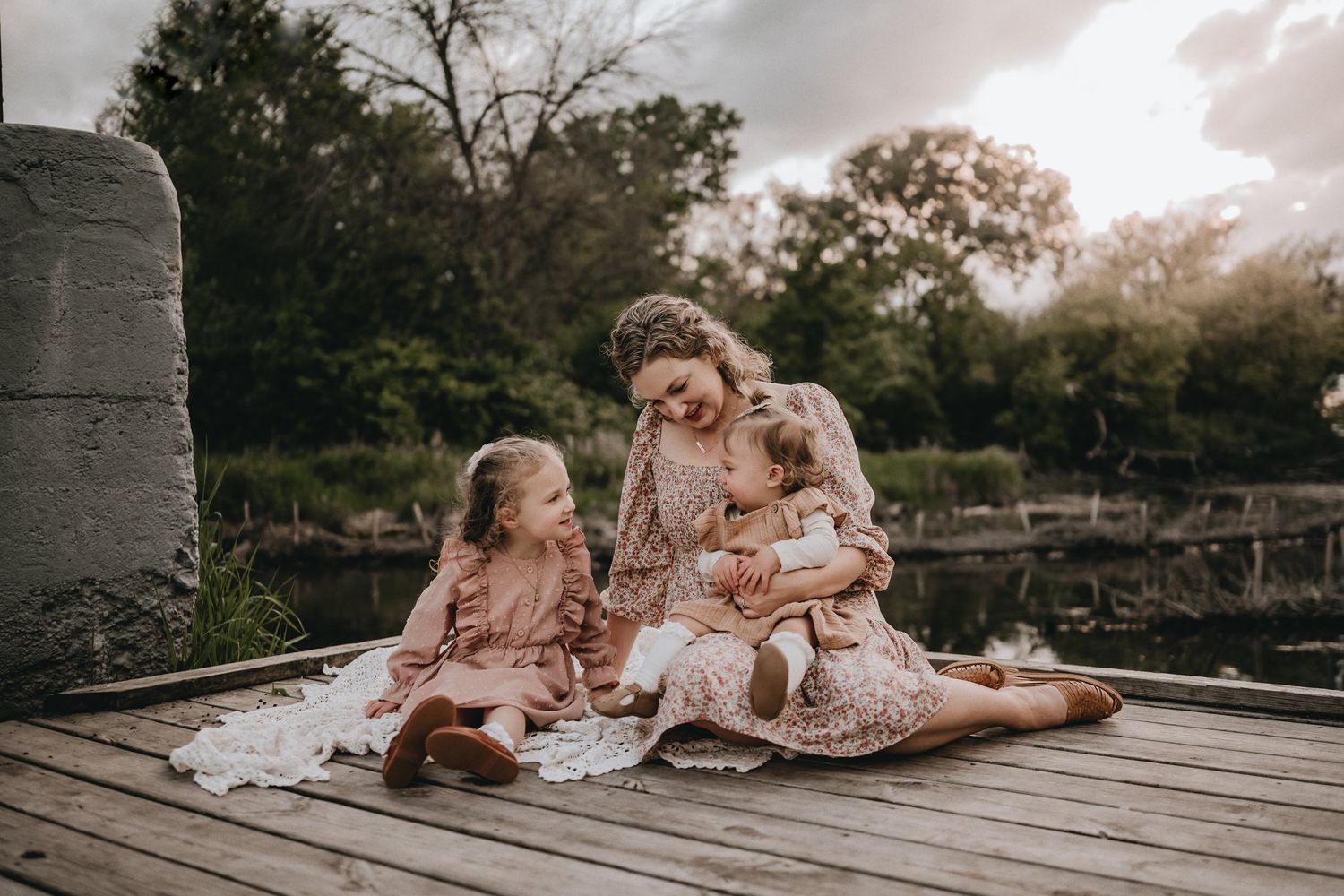 A tender family moment captured on a wooden dock by a lake.