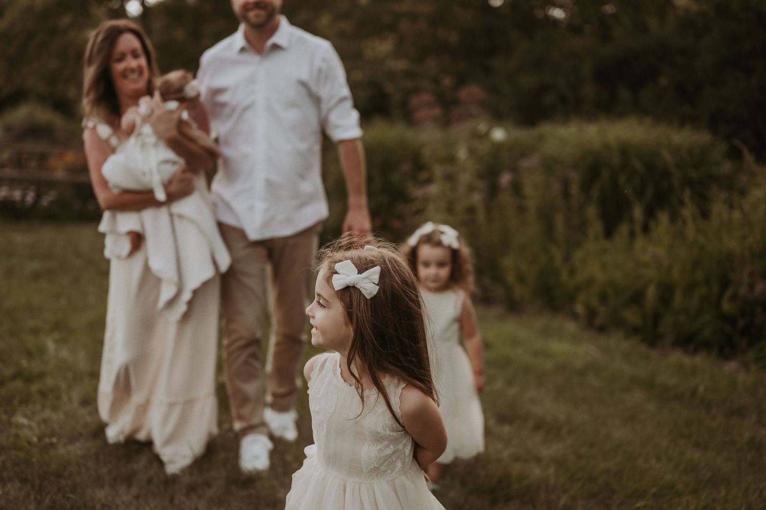 A family in white outfits enjoys a candid moment together in a garden setting during golden hour.