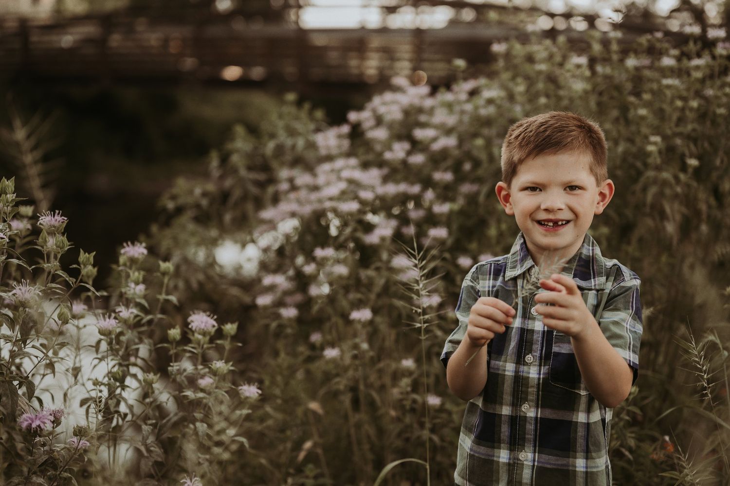 Child in plaid shirt shows joyful expression while playing in field of wildflowers.
