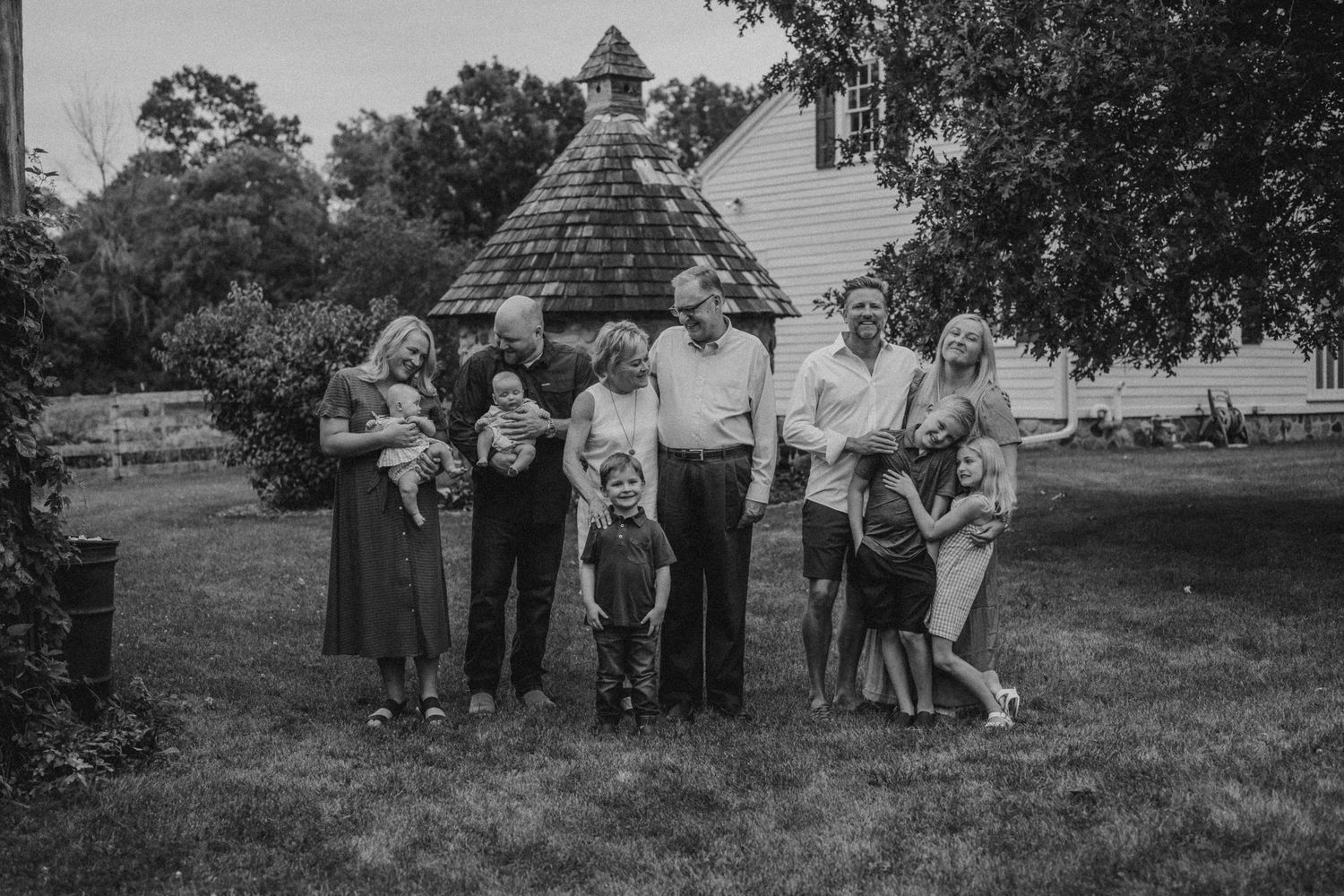 Black and white photo of extended family posing together on grassy lawn near historic buildings.