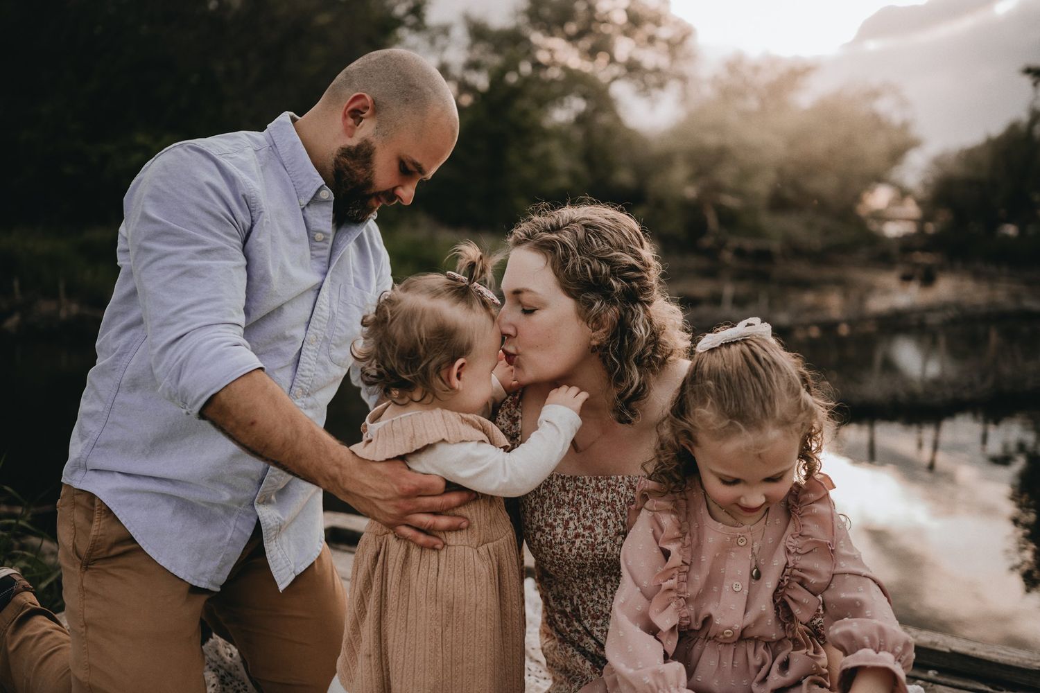 Family shares tender moment together by a lake at sunset in muted earth tones.
