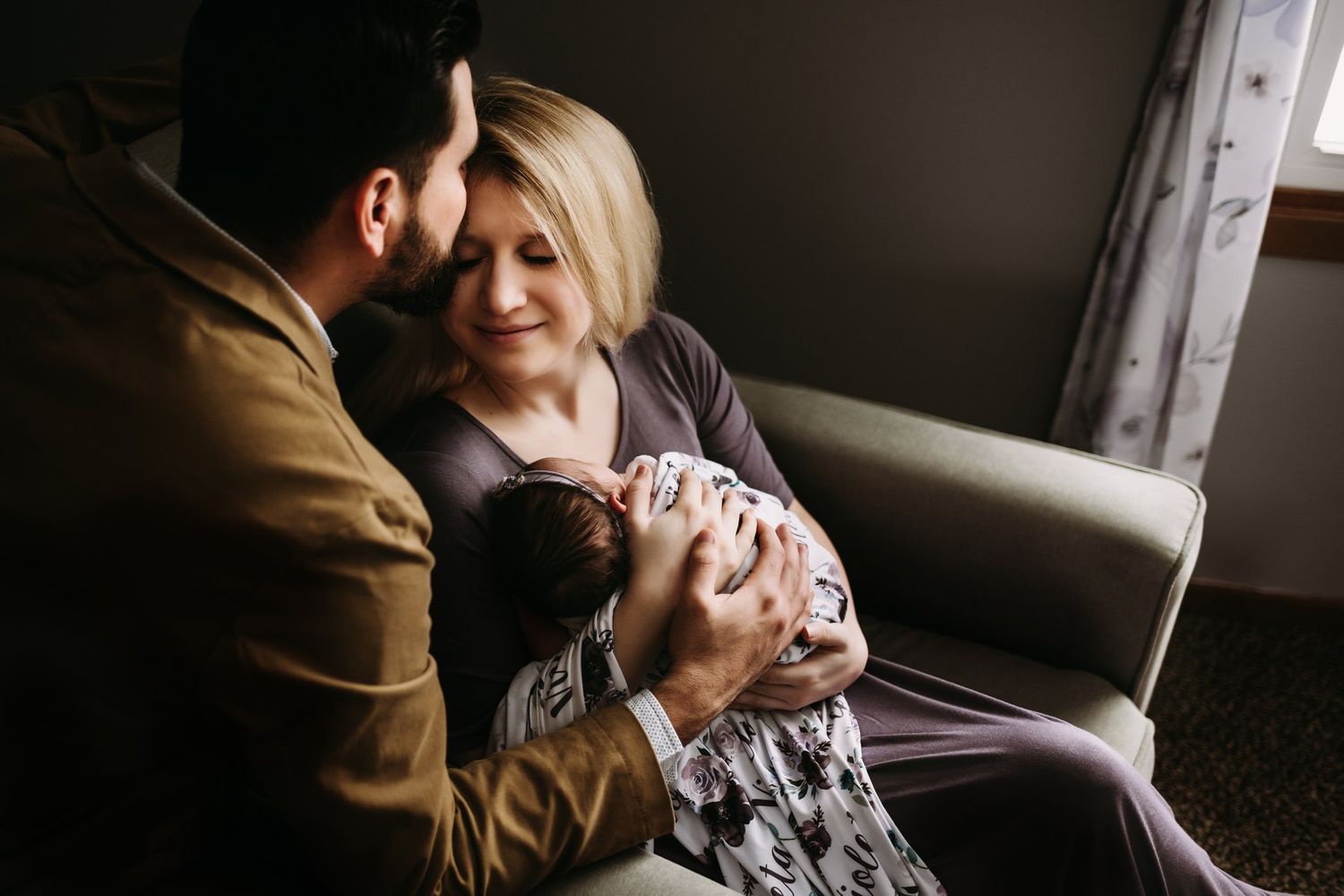 Tender family moment with new baby being held in living room chair.