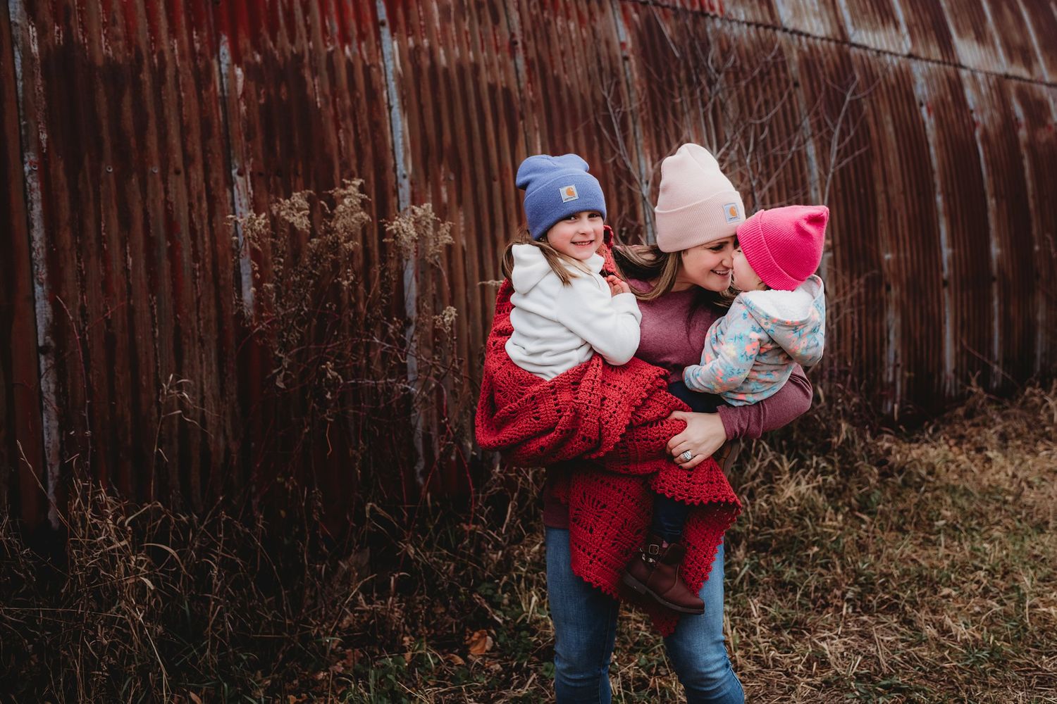 Candid family moment in front of rustic barn during winter photo session.
