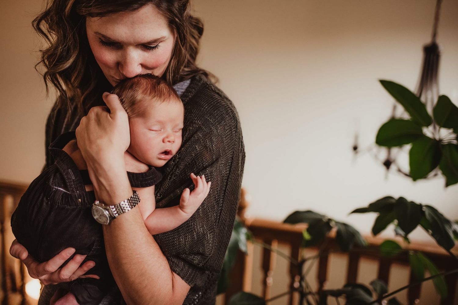 Intimate moment captured as adult cradles sleeping infant while standing near houseplants.