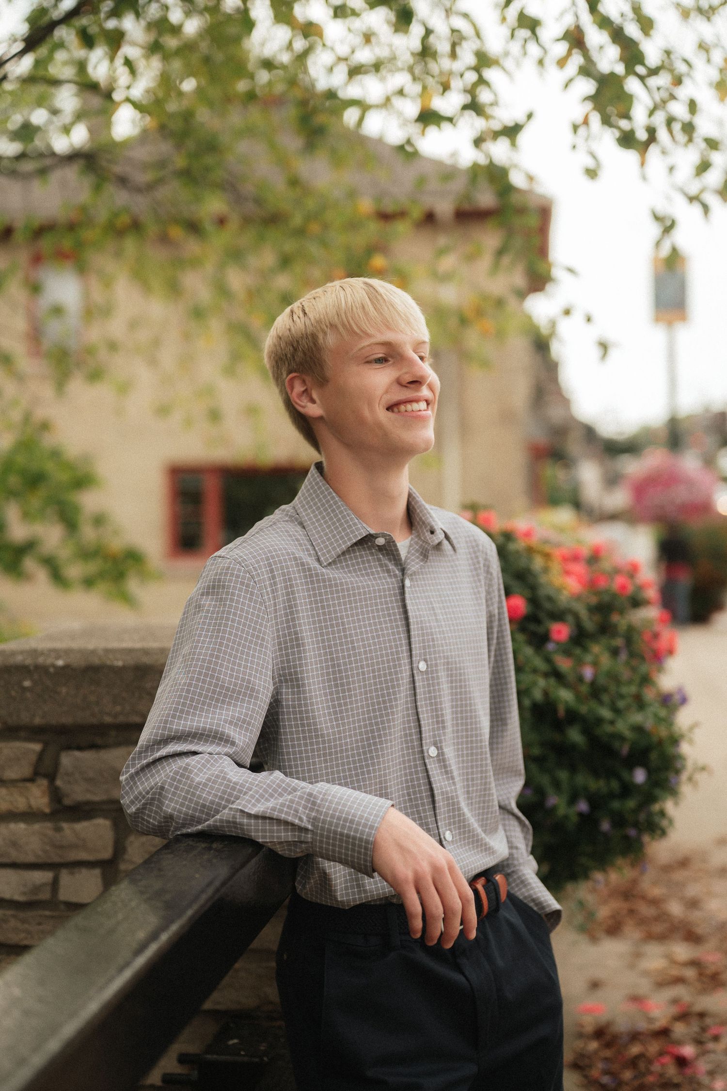 Portrait series in front of autumn foliage and stone wall wearing a checkered button-down shirt.