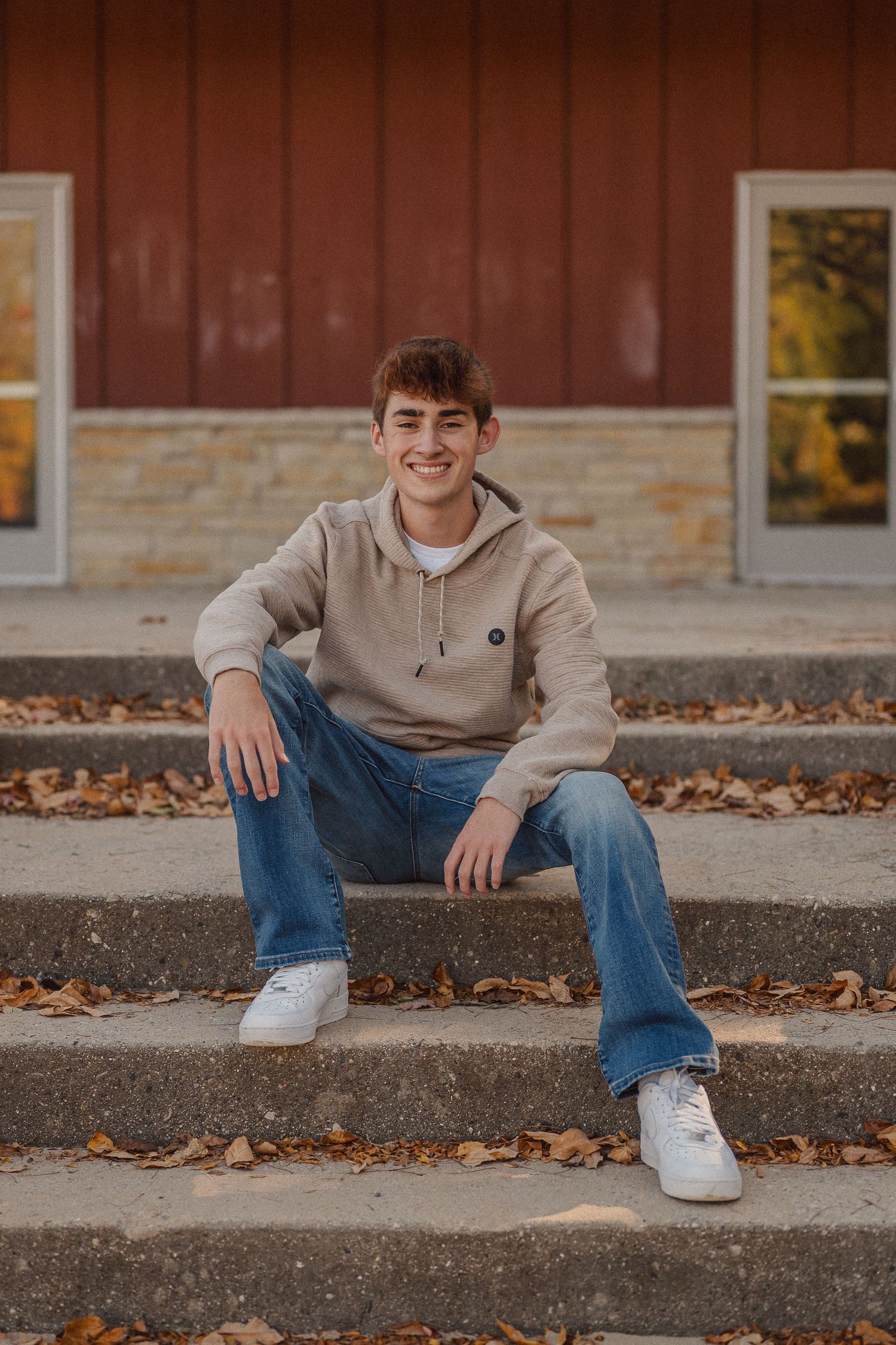 Person in beige sweatshirt and jeans sitting on concrete steps with fallen autumn leaves nearby.
