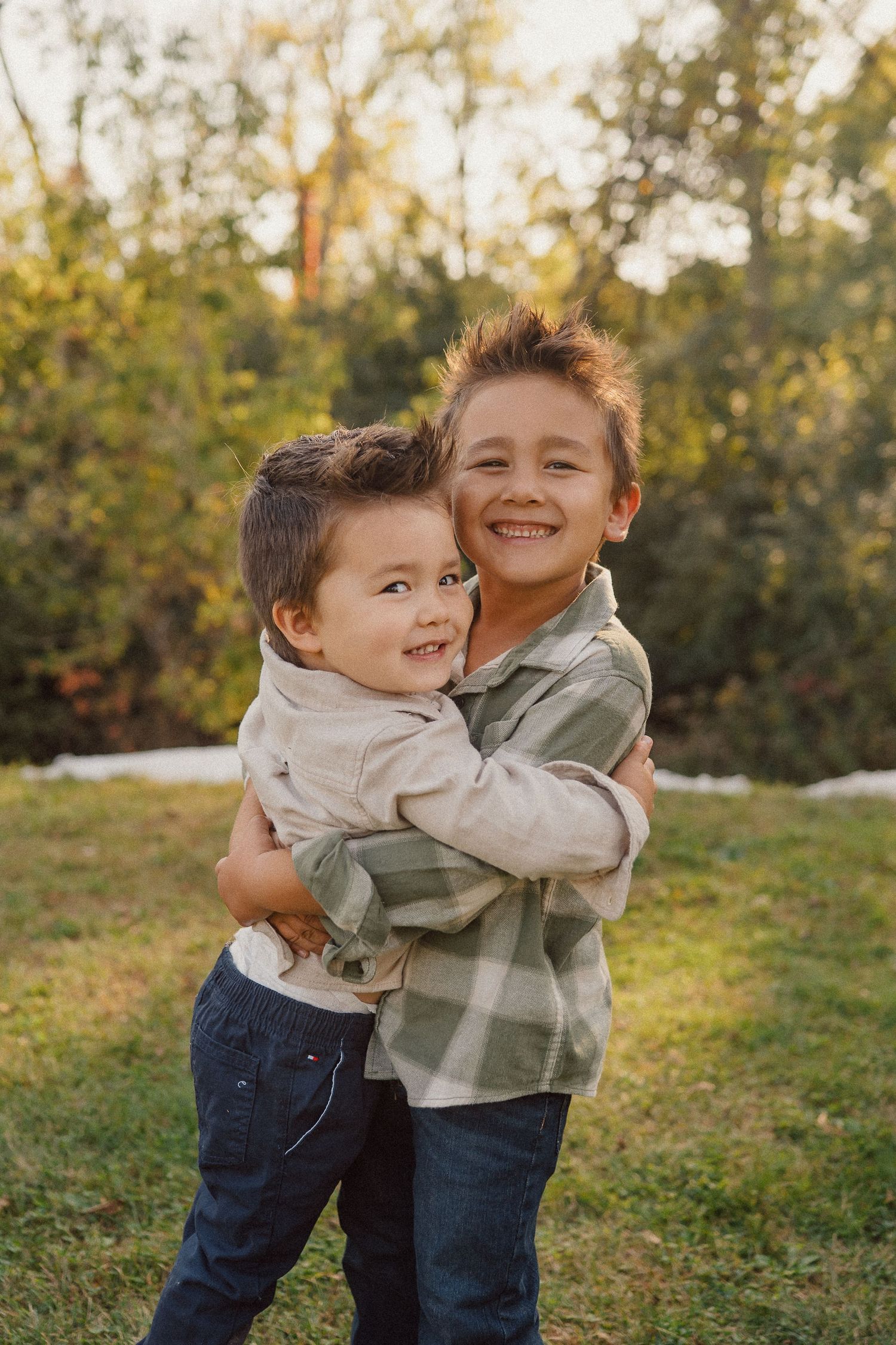 Two young children playing and hugging outdoors on a grassy hill at sunset.