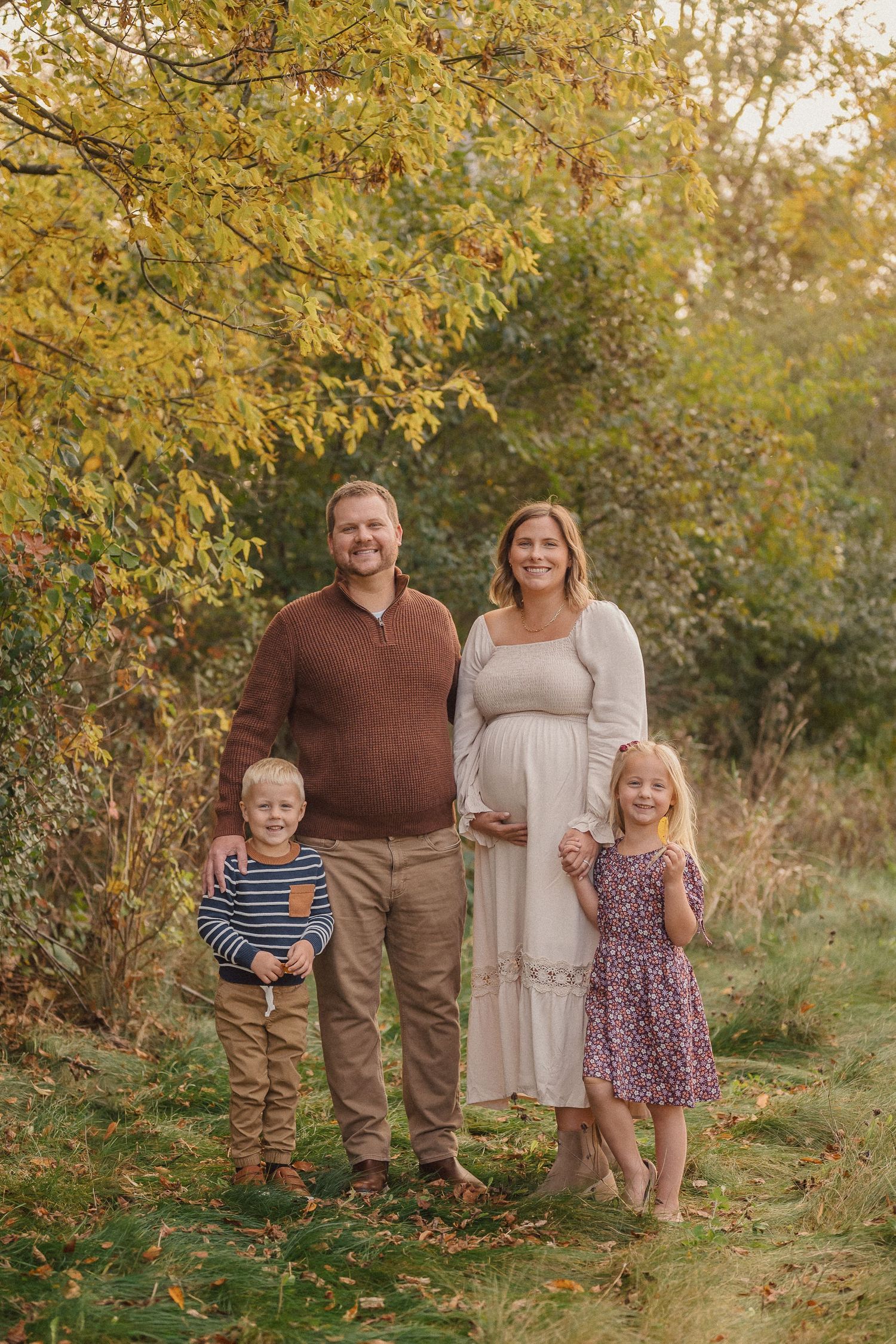 A family poses together outdoors on an autumn day with golden leaves in the background.