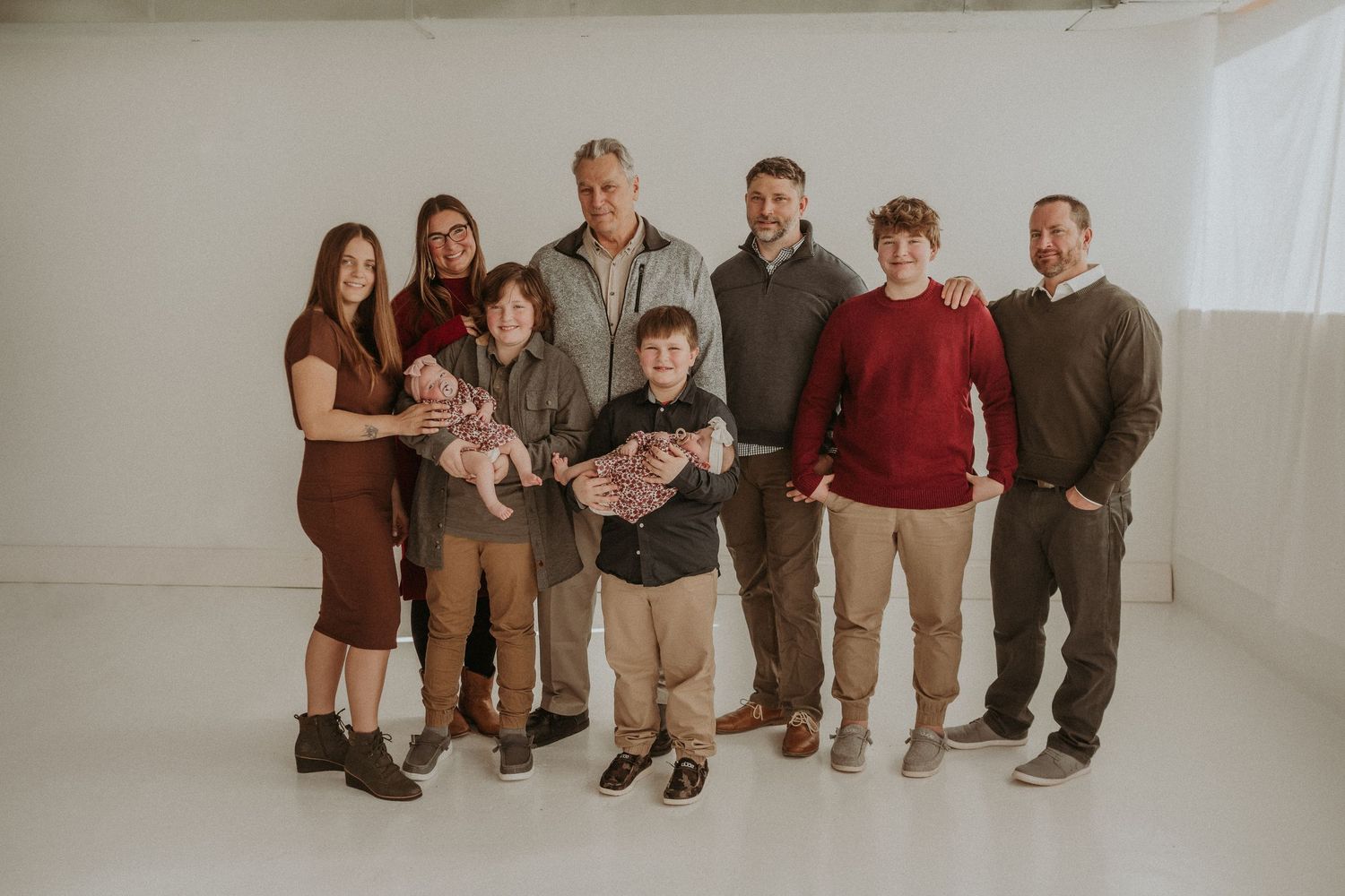 Family portrait with multiple generations wearing coordinated earth tones in white studio space.