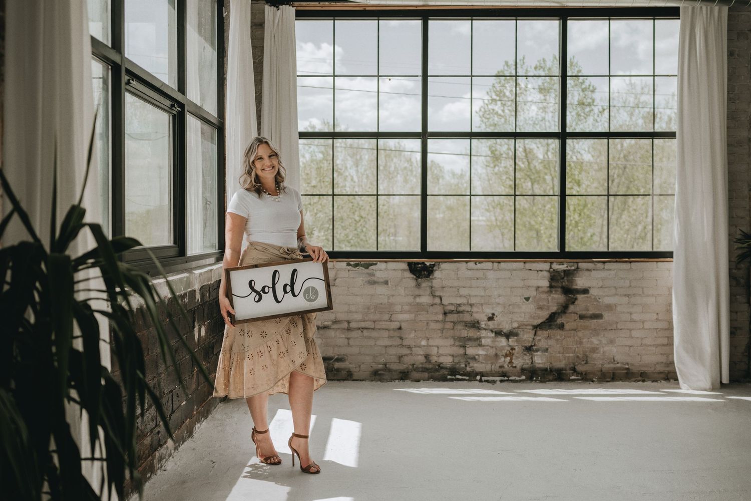 Woman in casual outfit displays wooden sign in bright industrial space.